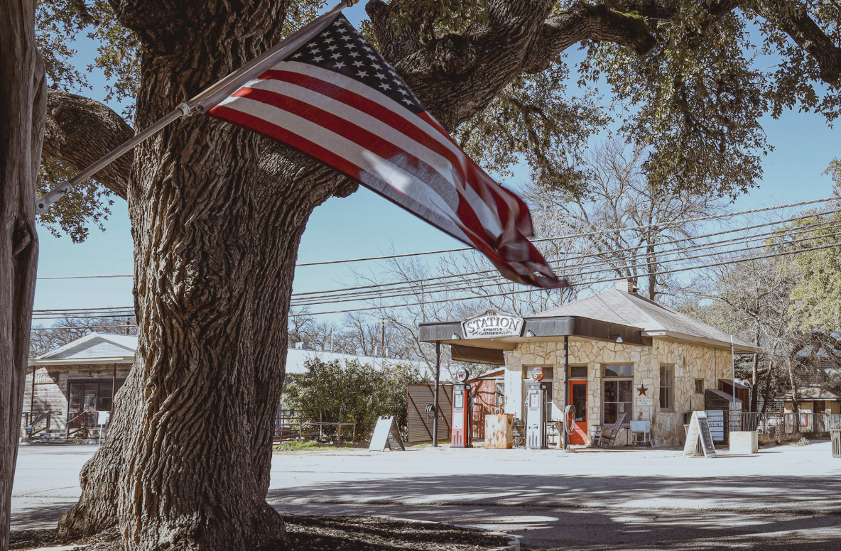 American flag on an oak tree beside a historic stone building in Dripping Springs, TX