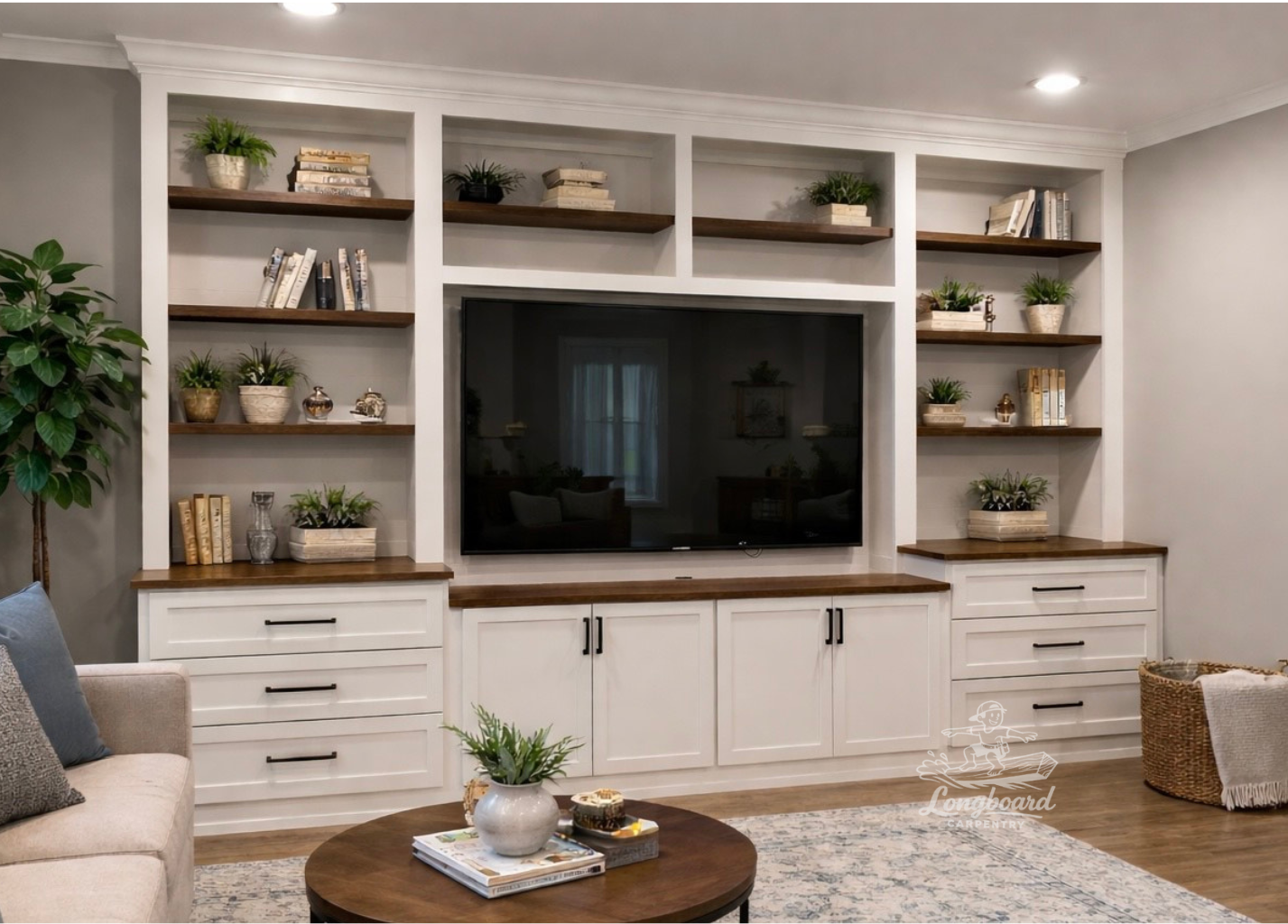 Living room with a custom built-in, painted white with wood entertainment center, houseplants, books, TV, beige sofa, coffee table, and woven basket.