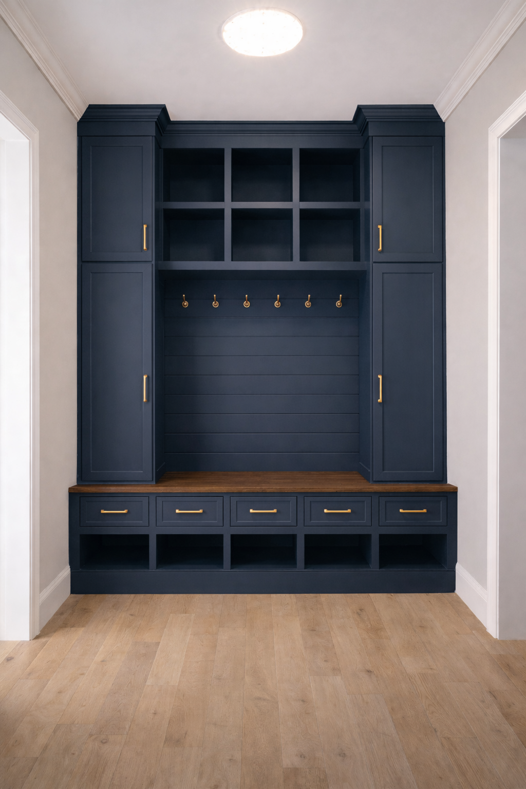 A navy blue built-in entryway storage and coat rack with cabinets, open cubbies, hooks, and drawers on a light hardwood floor.