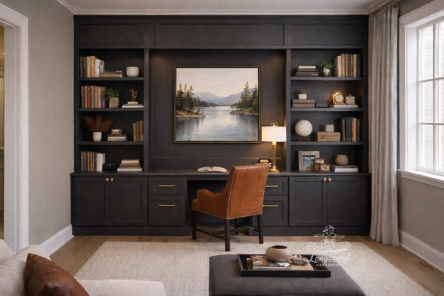 Home office with painted black built-in bookshelf by Longboard Carpentry IL, framed landscape painting, desk with open book, brown leather chair, window with curtains, beige area rug, and decorative objects.