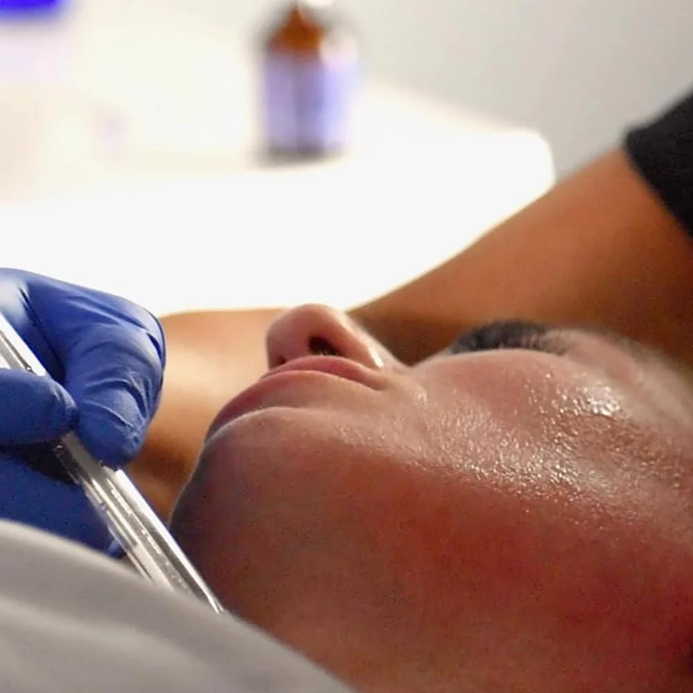 A person lying down receiving an injection in their upper arm from a healthcare professional wearing blue gloves.
