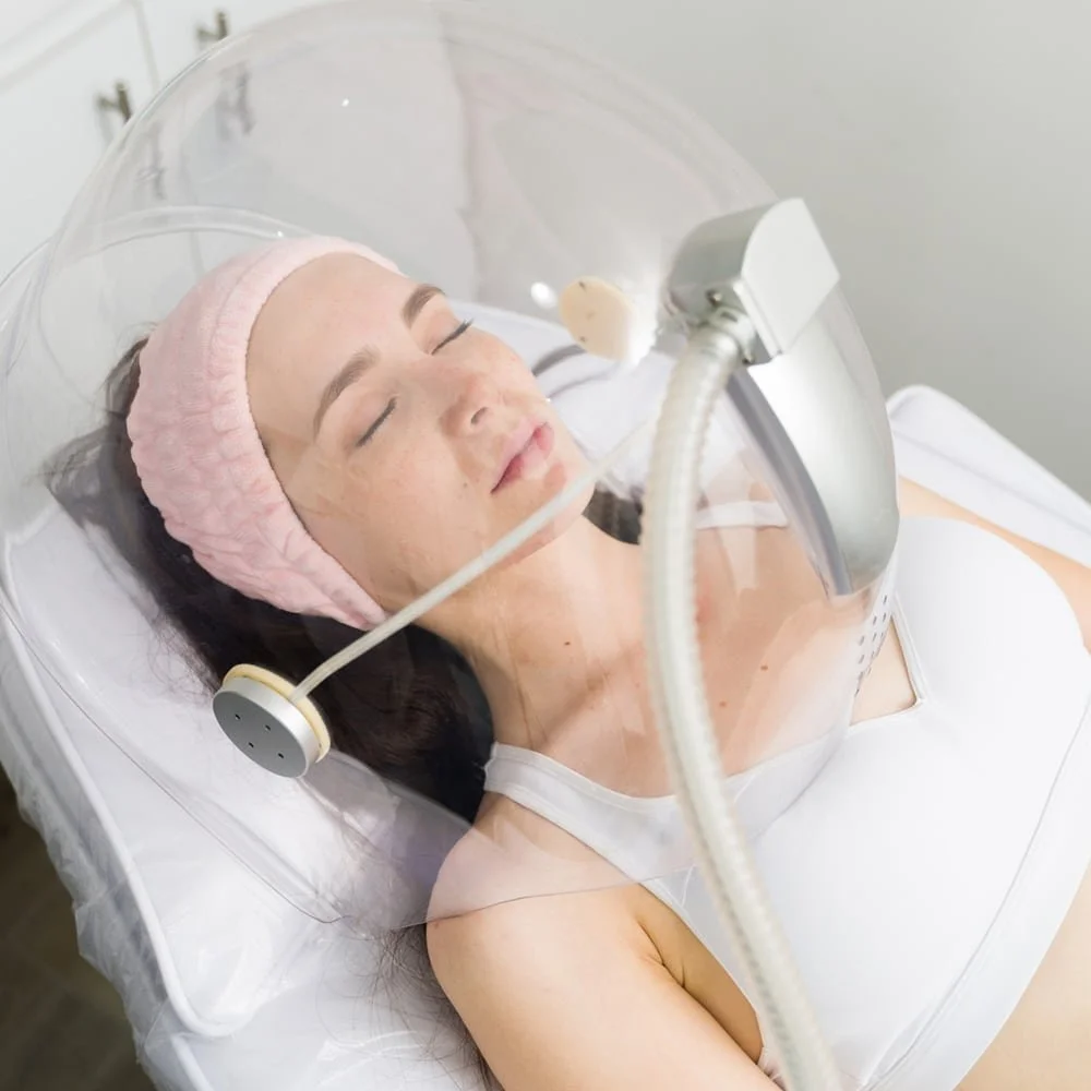 Client relaxing under the OxiVelour oxygen dome during facial treatment