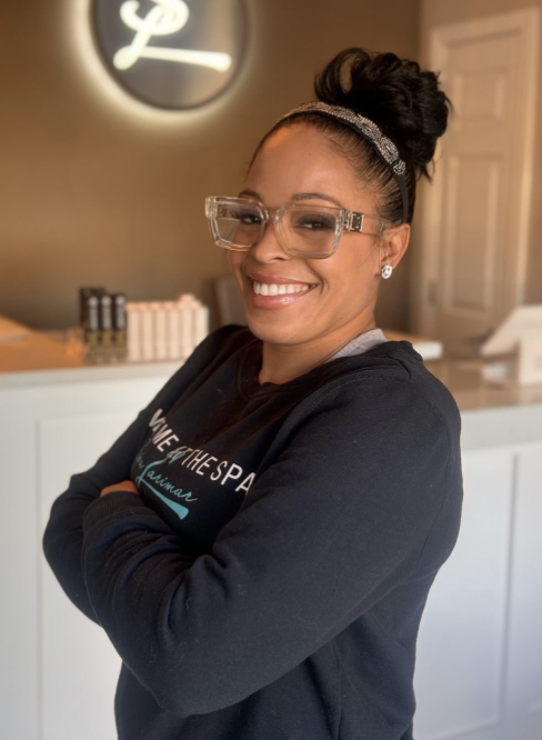 Maria with glasses and earrings, wearing a headband and black sweatshirt, standing inside Spa Larimar's waiting area.