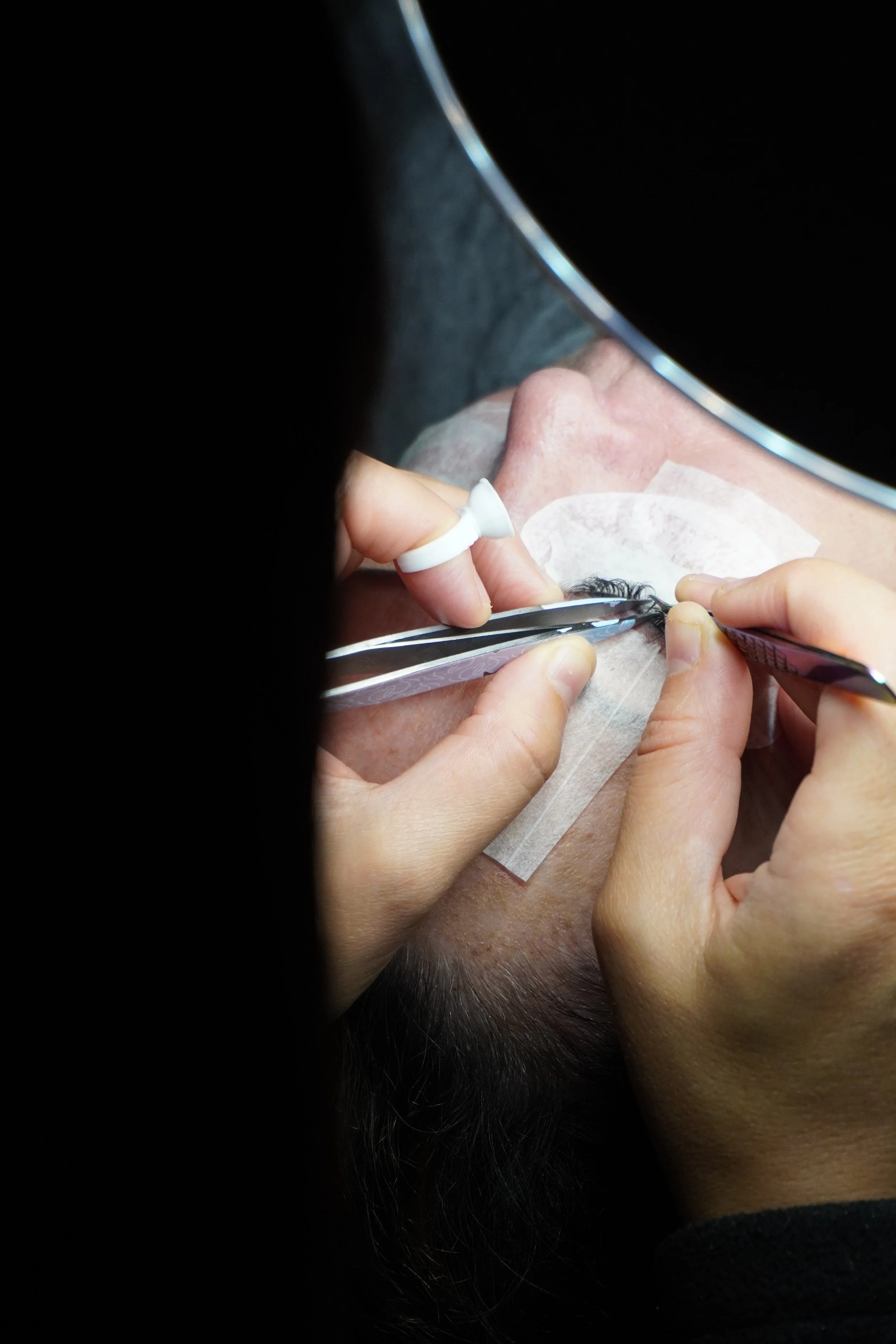 Close-up of a person getting eyelash extensions, with technician applying false eyelashes to a client's eye.