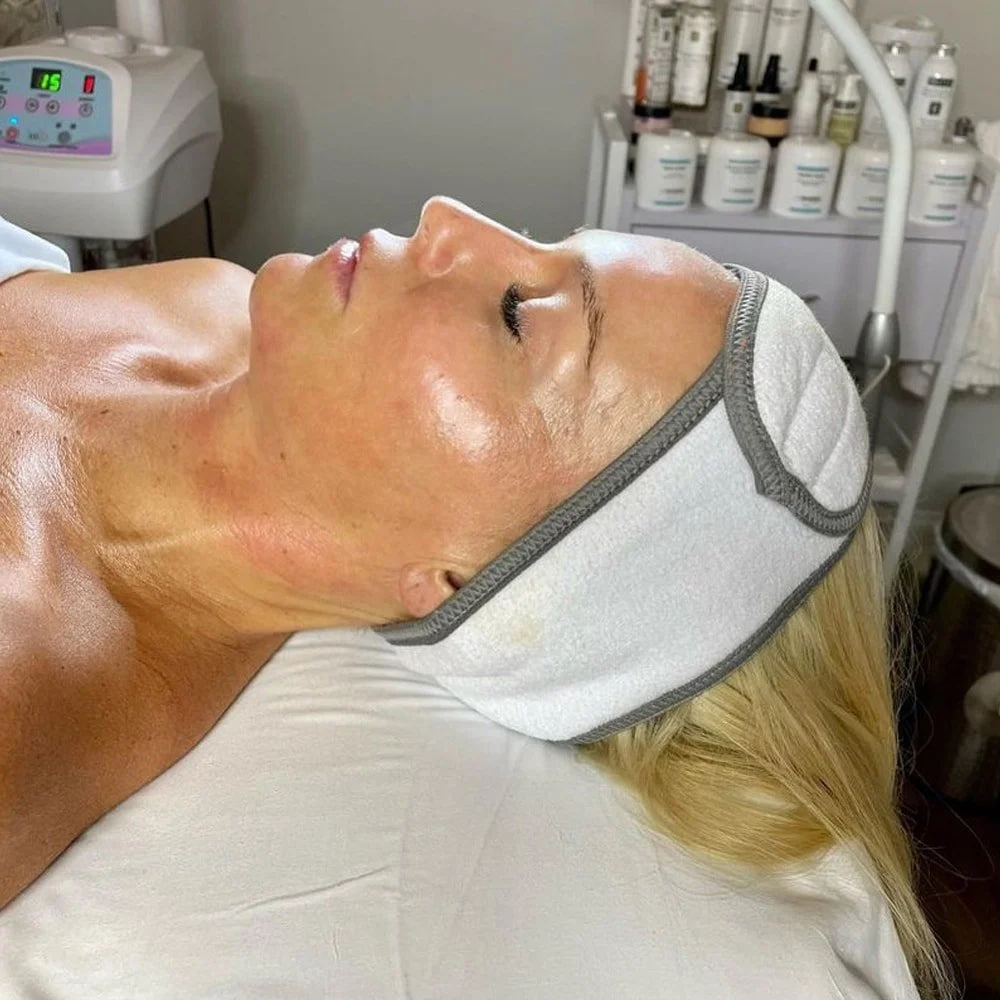 A woman lying down with a facial mask cap, receiving a facial treatment in a spa or clinic.