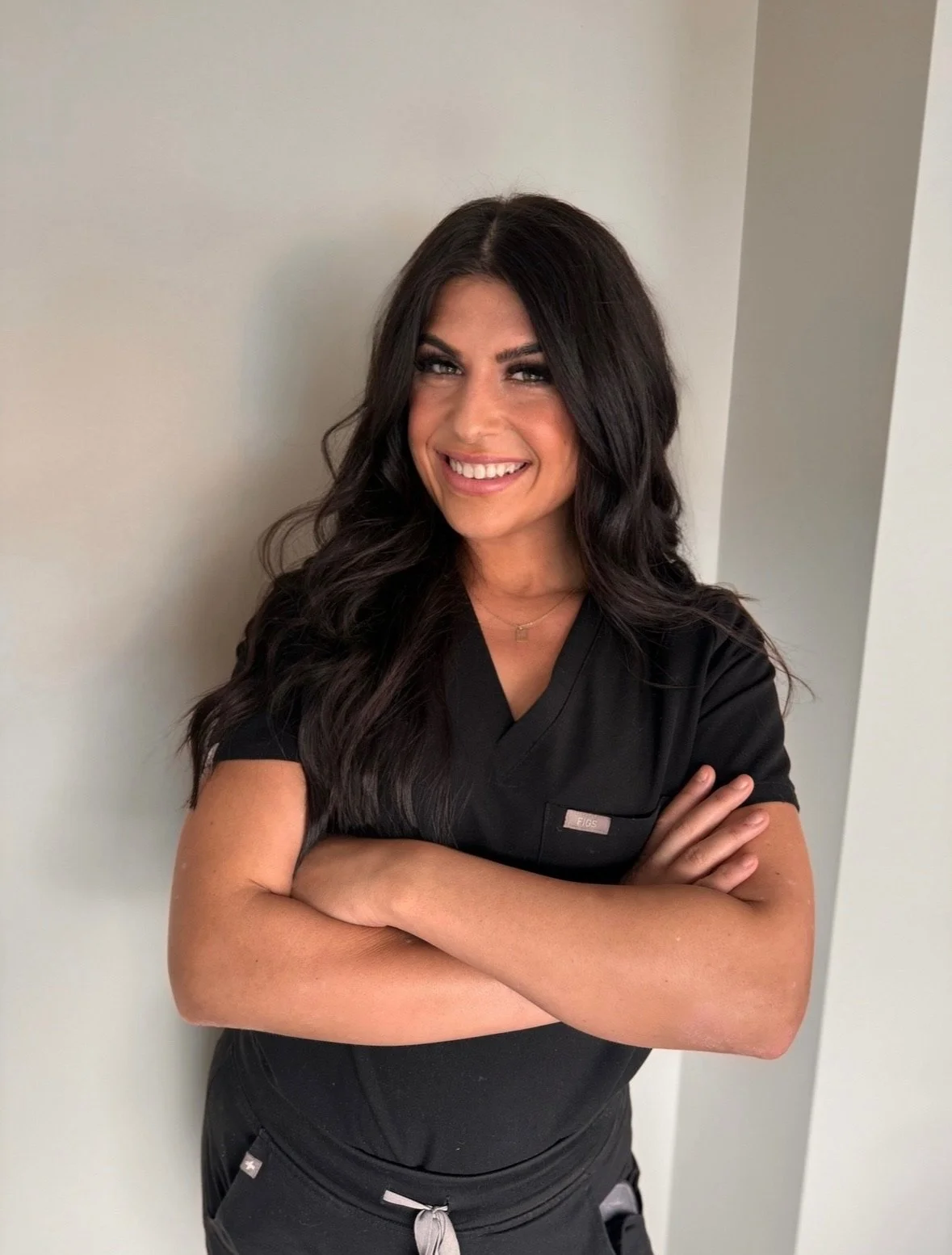 Cassidy wearing black scrubs, standing crossed arms against a plain wall.