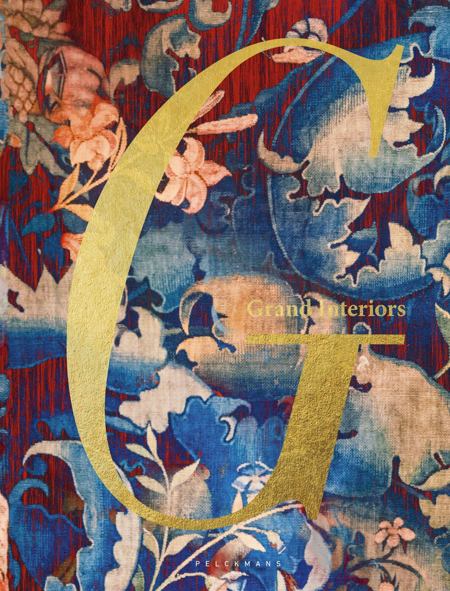 Une affiche avec un fond en tissu florale de couleurs rouge, bleu, rose et beige. Sur l'affiche, un grand logo doré en forme de G, avec le texte "Grand Interiors" et la signature "PELCKMANS".