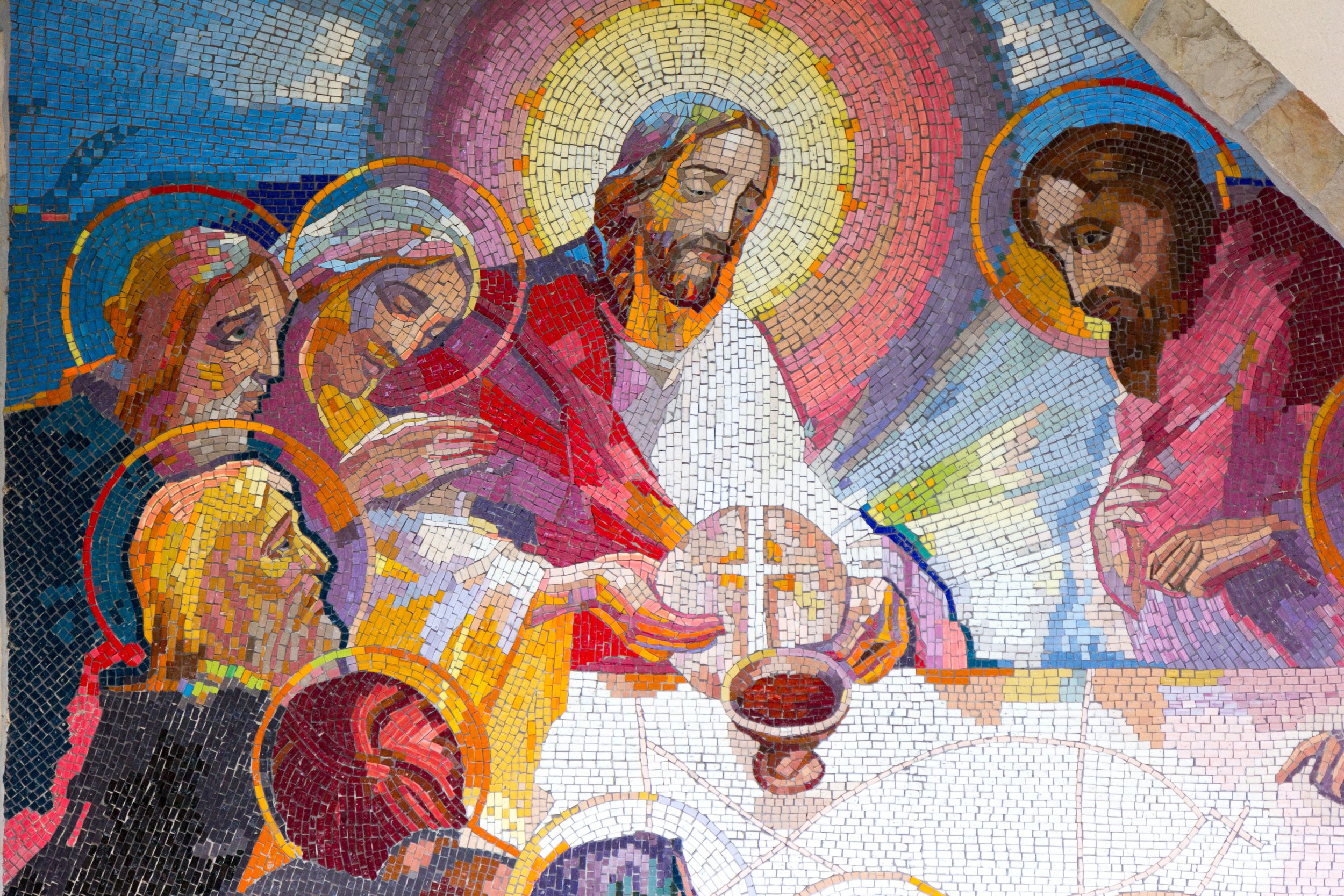 Colorful mosaic depicting the last supper with Jesus Christ at the center surrounded by apostles, holding a cup and sharing bread, with vibrant background hues.