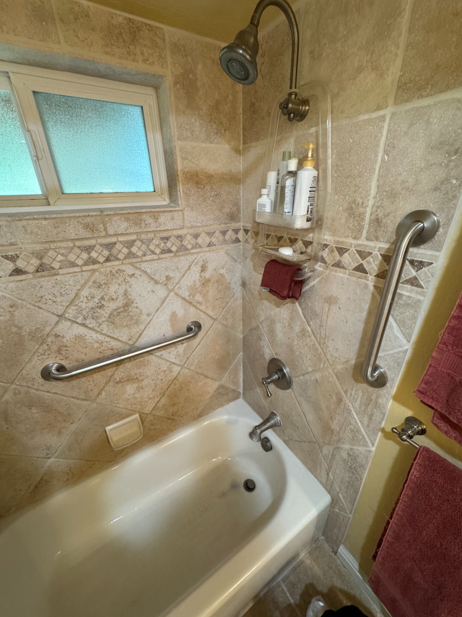 Stainless steel grab bars installed in tub shower with stone tile, residential accessibility modification