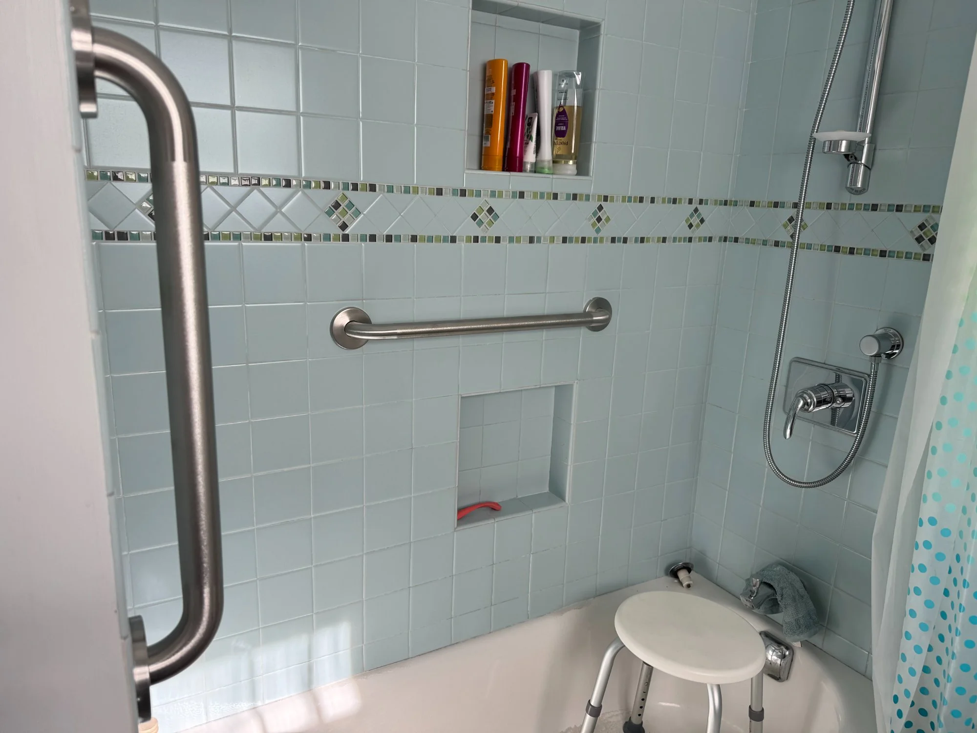 Stainless grab bar installed beside bathtub with blue tile, residential safety modification