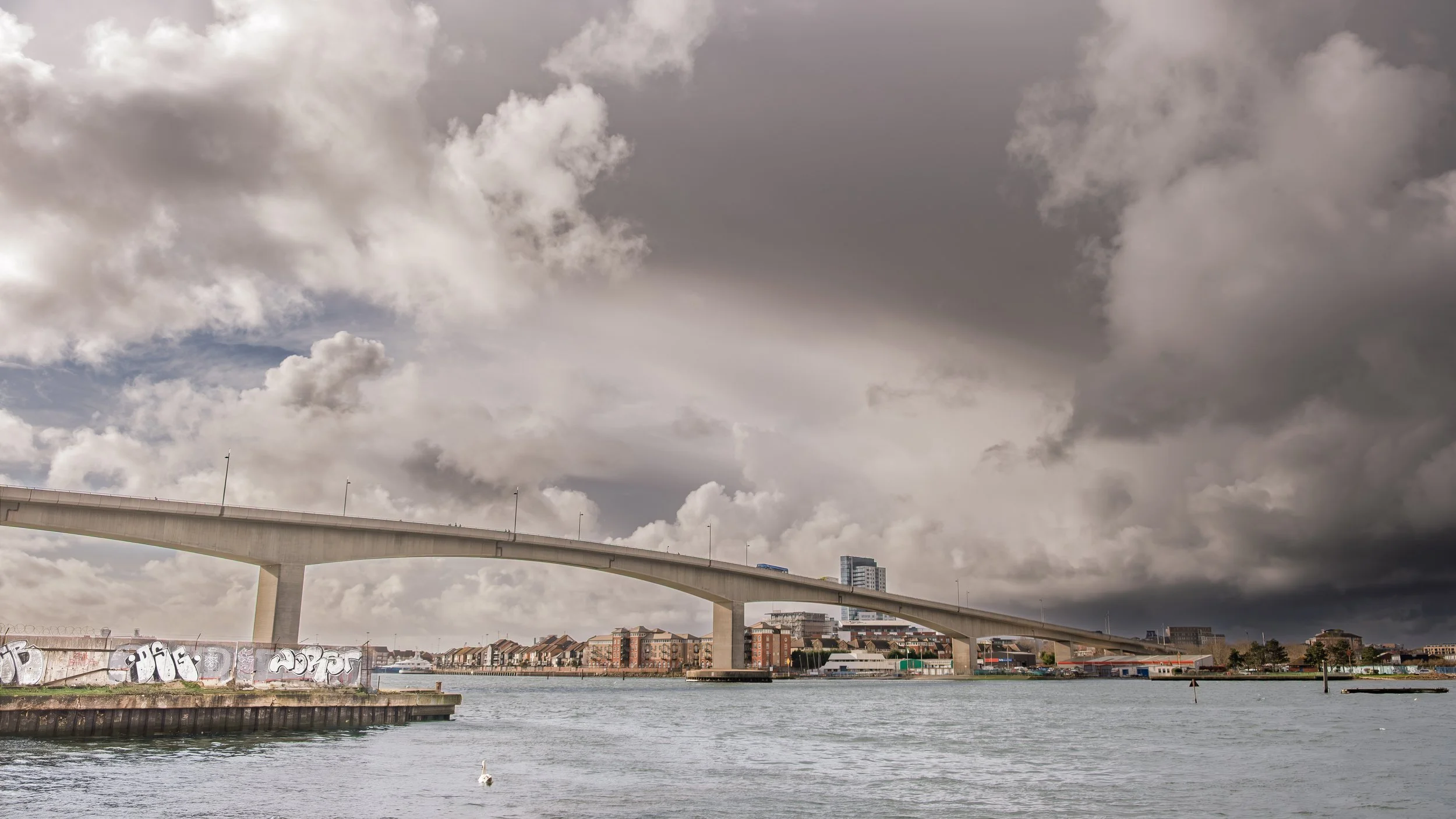 The Itchen bridge extends over a body of water with buildings and overcast skies in the background.