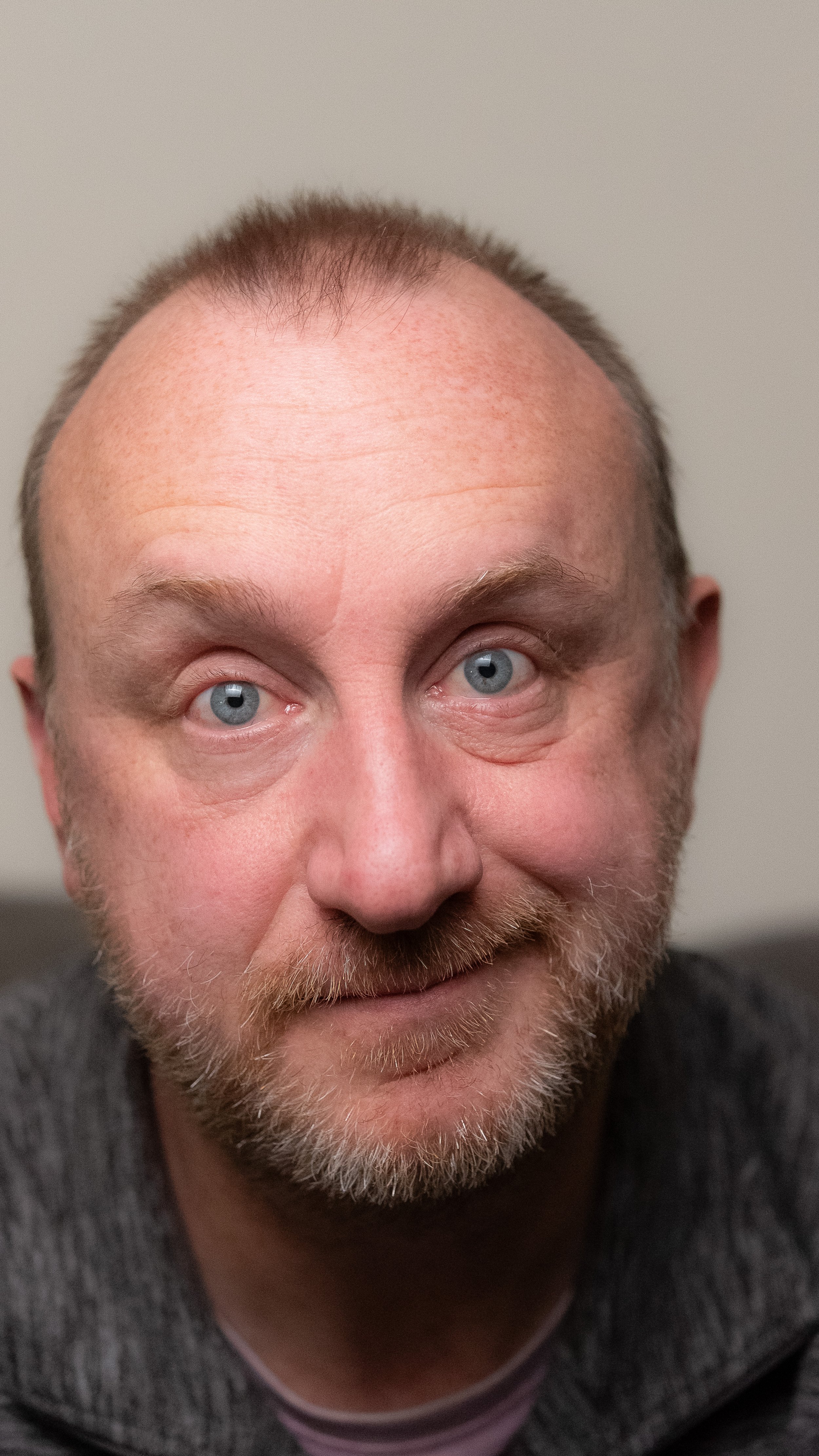 Close-up portrait of a middle-aged man with blue eyes, a light beard, and short hair, wearing a dark shirt.