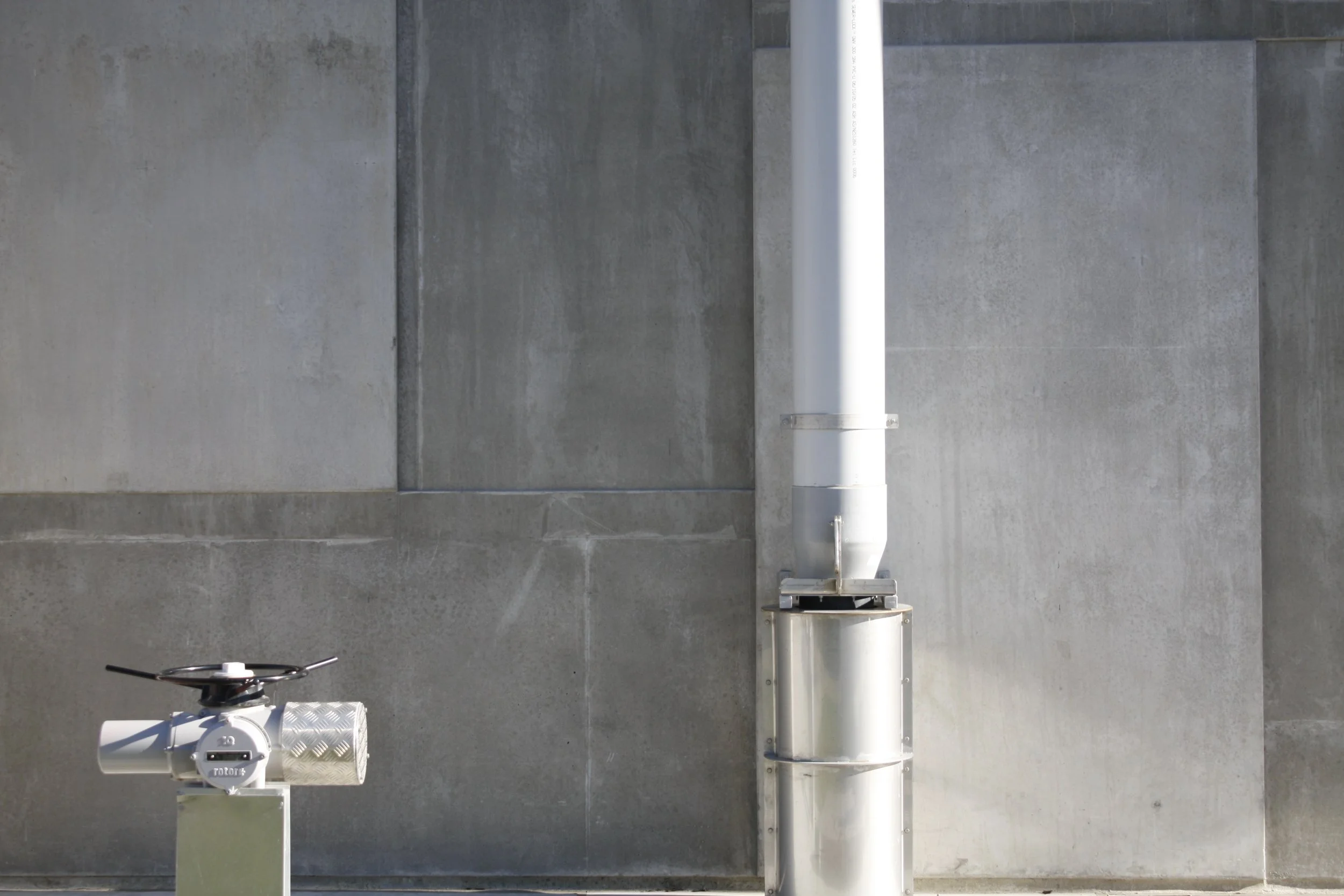 Metal pipe and valve against a concrete wall.