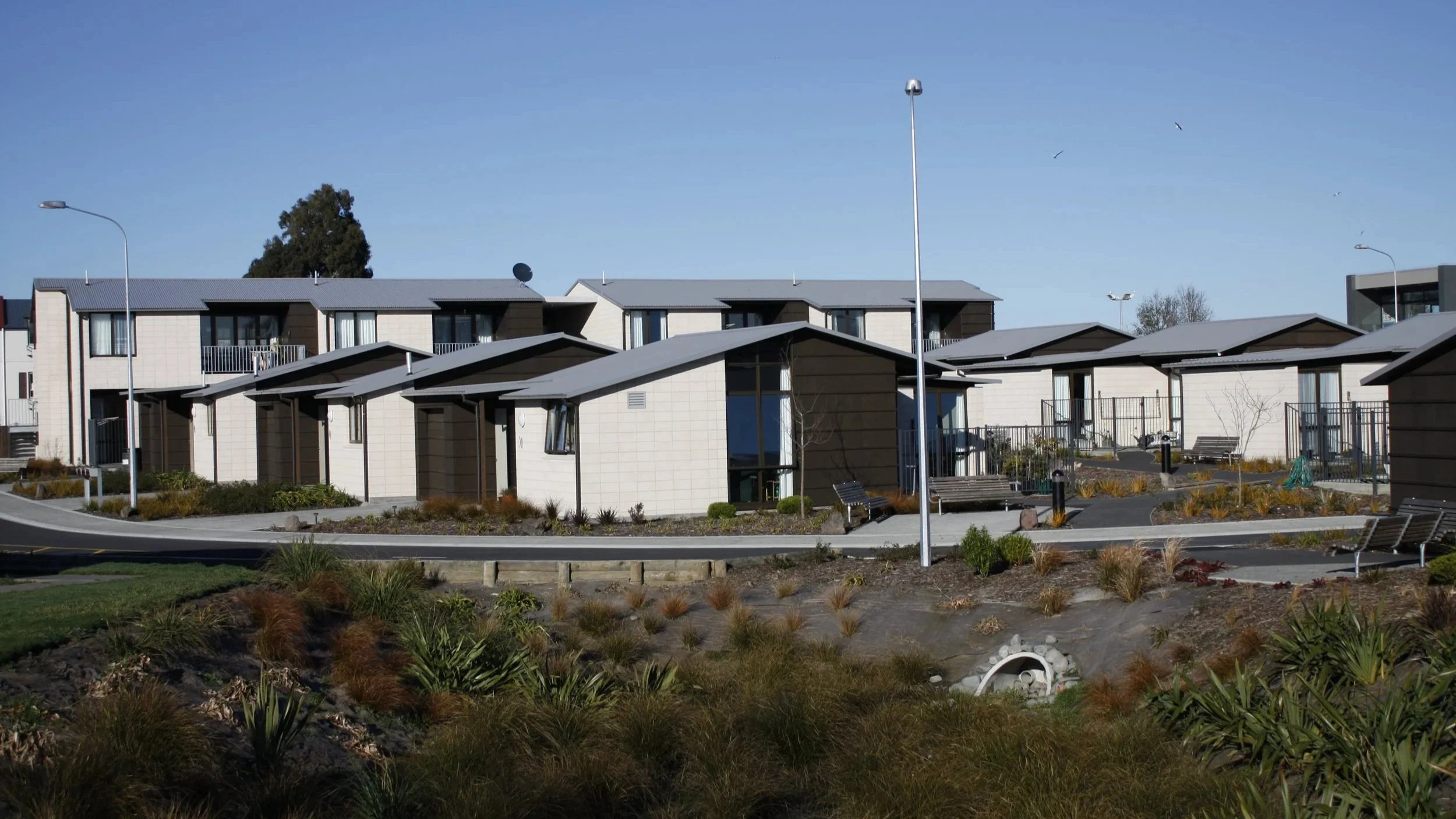 Modern residential apartments and townhouses with landscaped gardens and pathways under a clear blue sky.