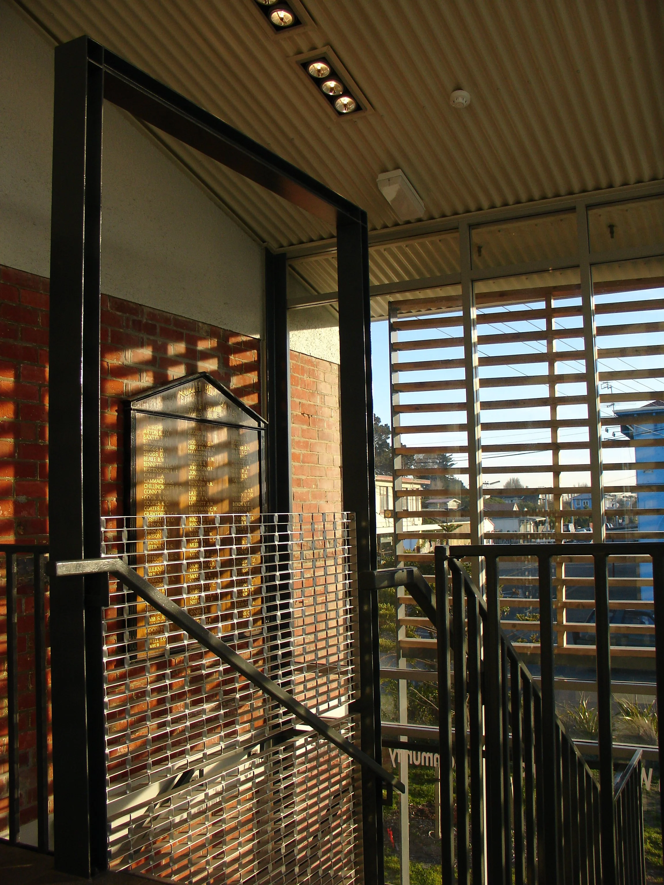 Photo of an entrance stairway with black metal rails, a brick wall, and a wooden slat wall outside with houses and trees visible in the background.