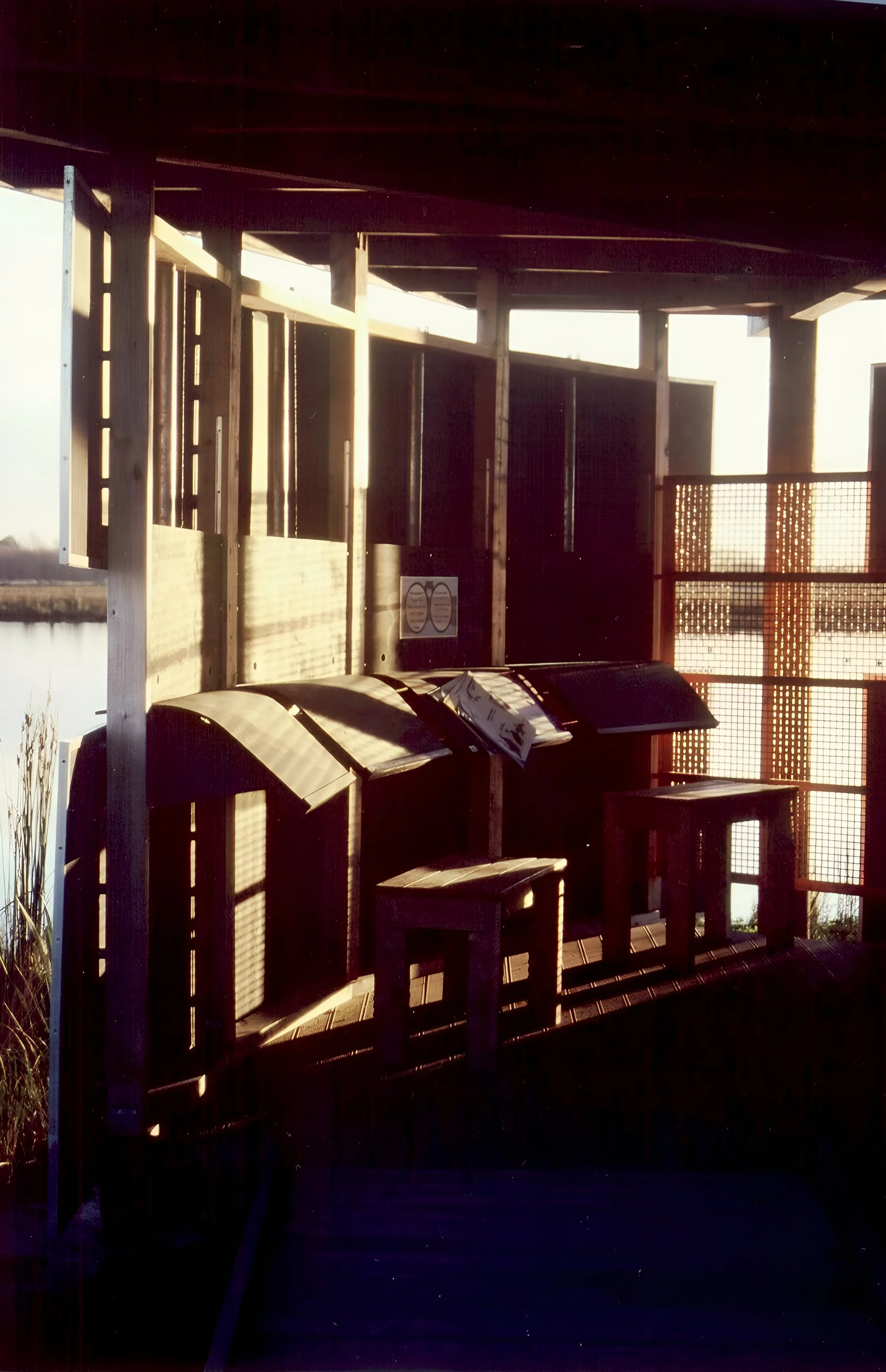 View of a love lock fence by a body of water at sunset, with wooden benches and a sign attached to the fence.