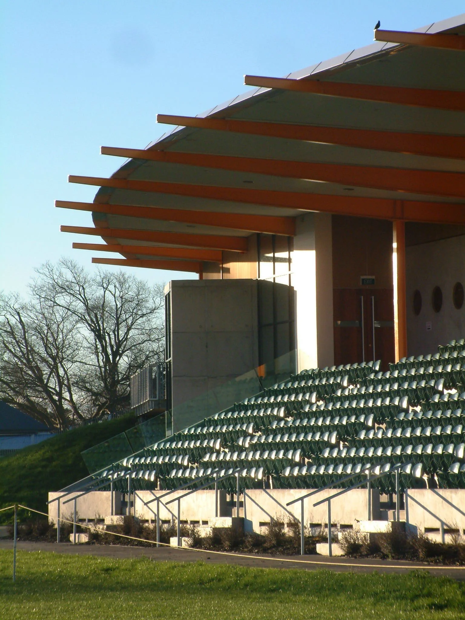 Empty outdoor auditorium with green seats and a modern building with an overhanging roof.