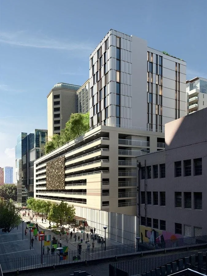 Modern multi-story commercial and residential buildings with trees and outdoor seating in an urban setting, clear blue sky.