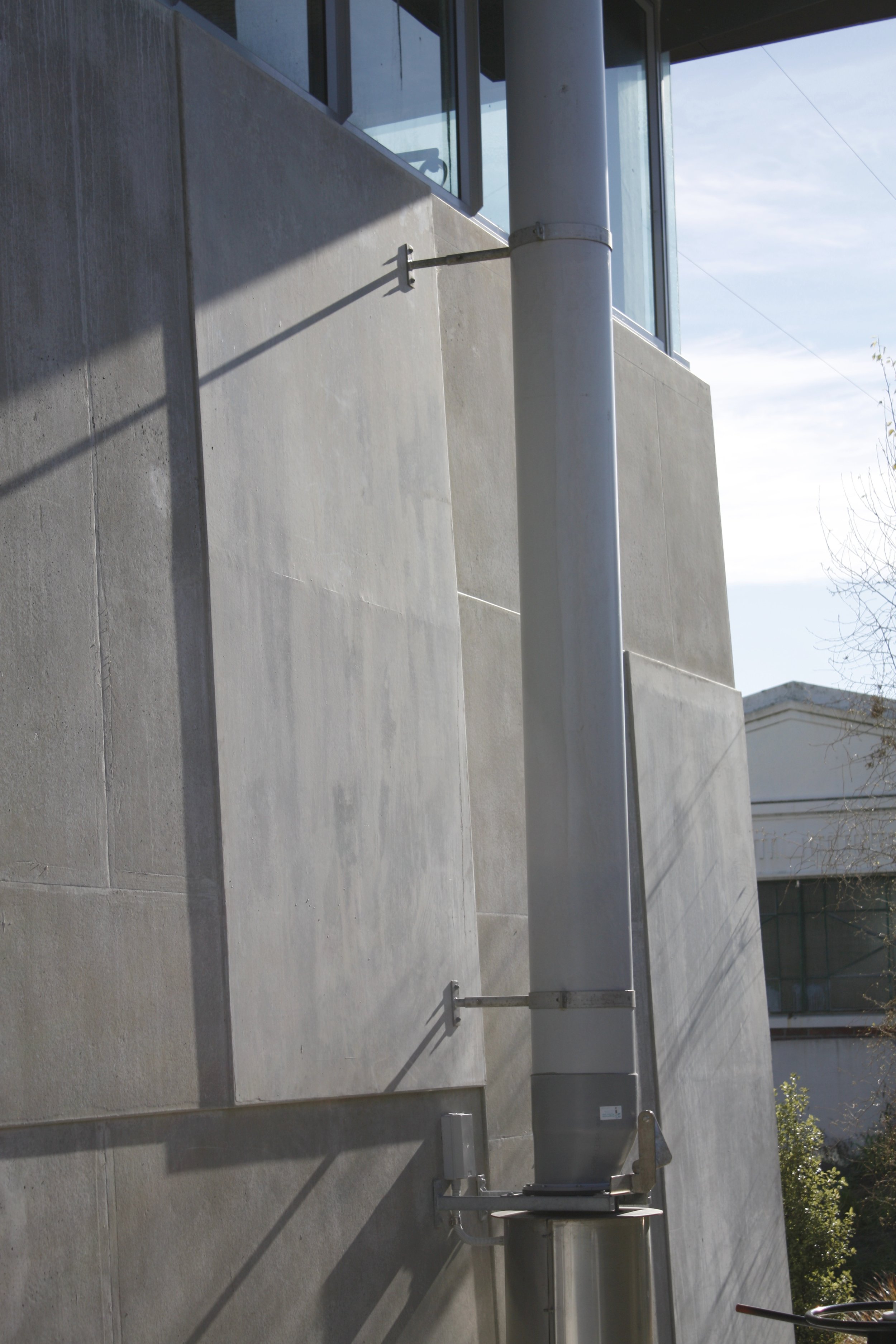 Outdoor modern building with concrete walls, large windows, and metal piping.