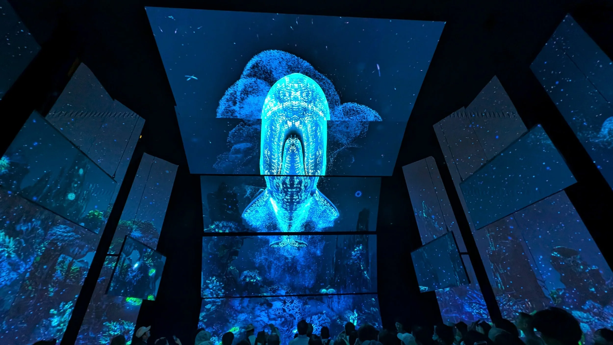 People inside an immersive digital art exhibit with large screens displaying a glowing blue whale and underwater scene.