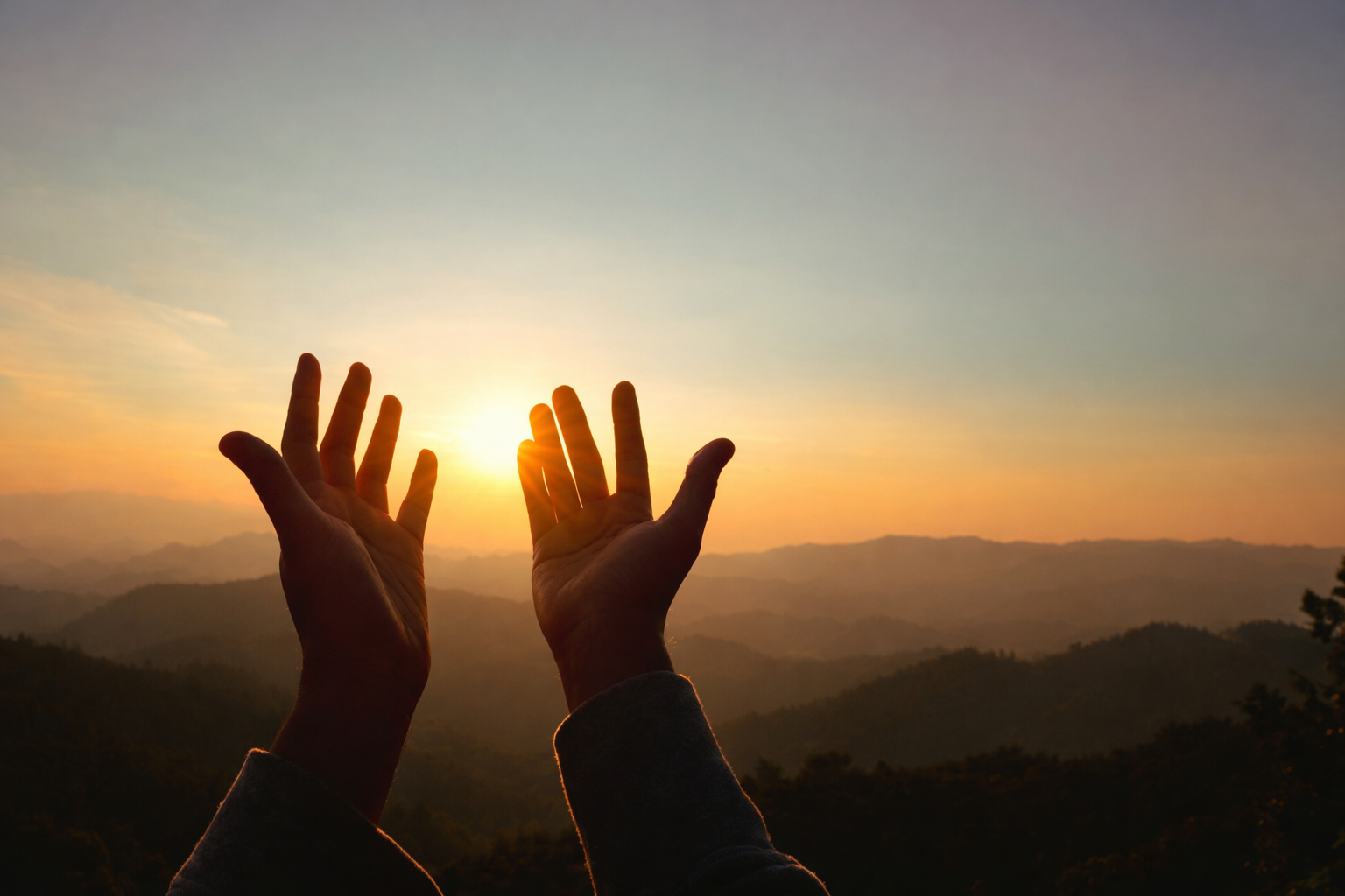 Hands reaching towards the sunset over a landscape of rolling hills.