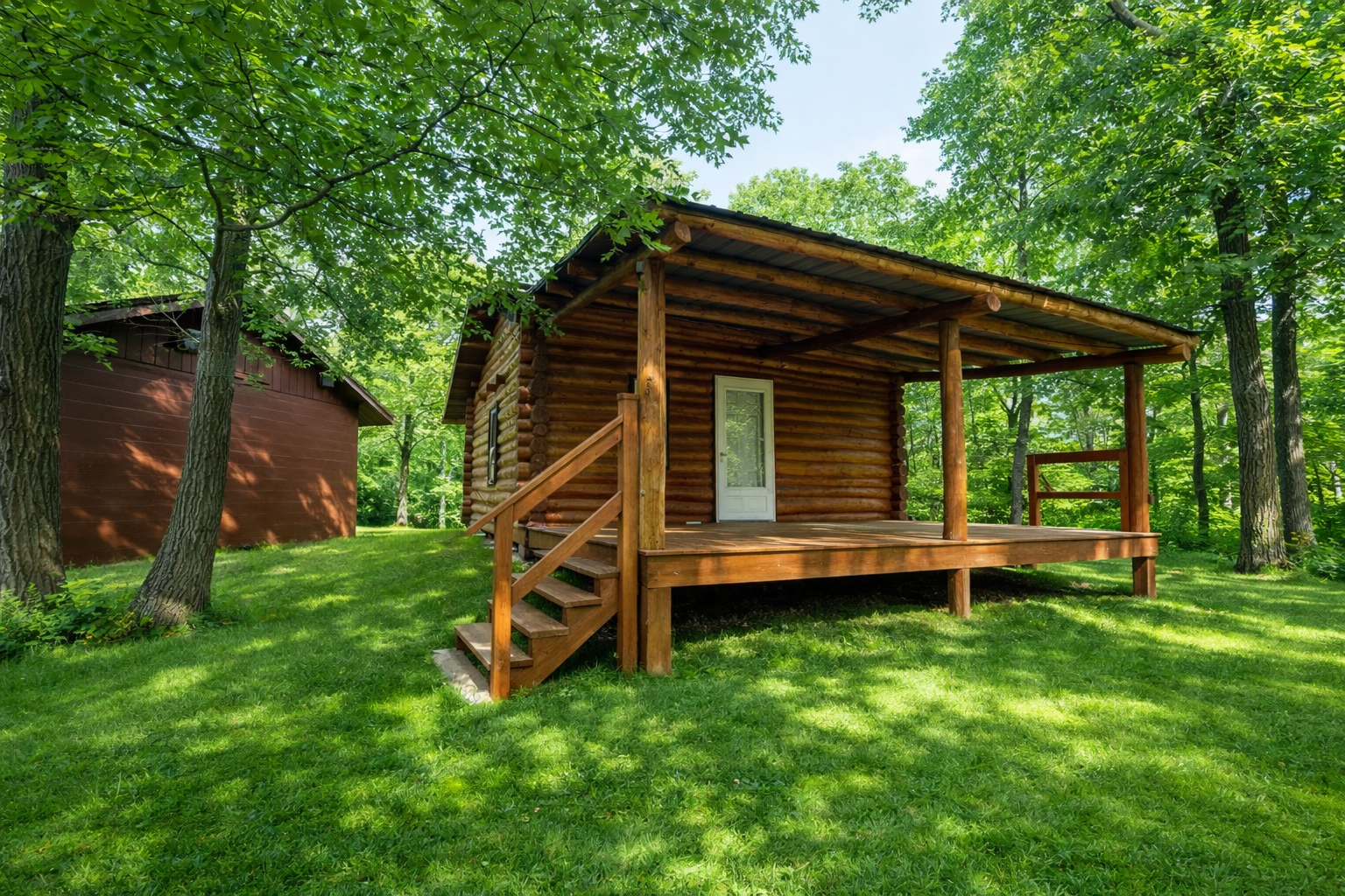 Wooden cabin with stairs and porch surrounded by green trees and grass.