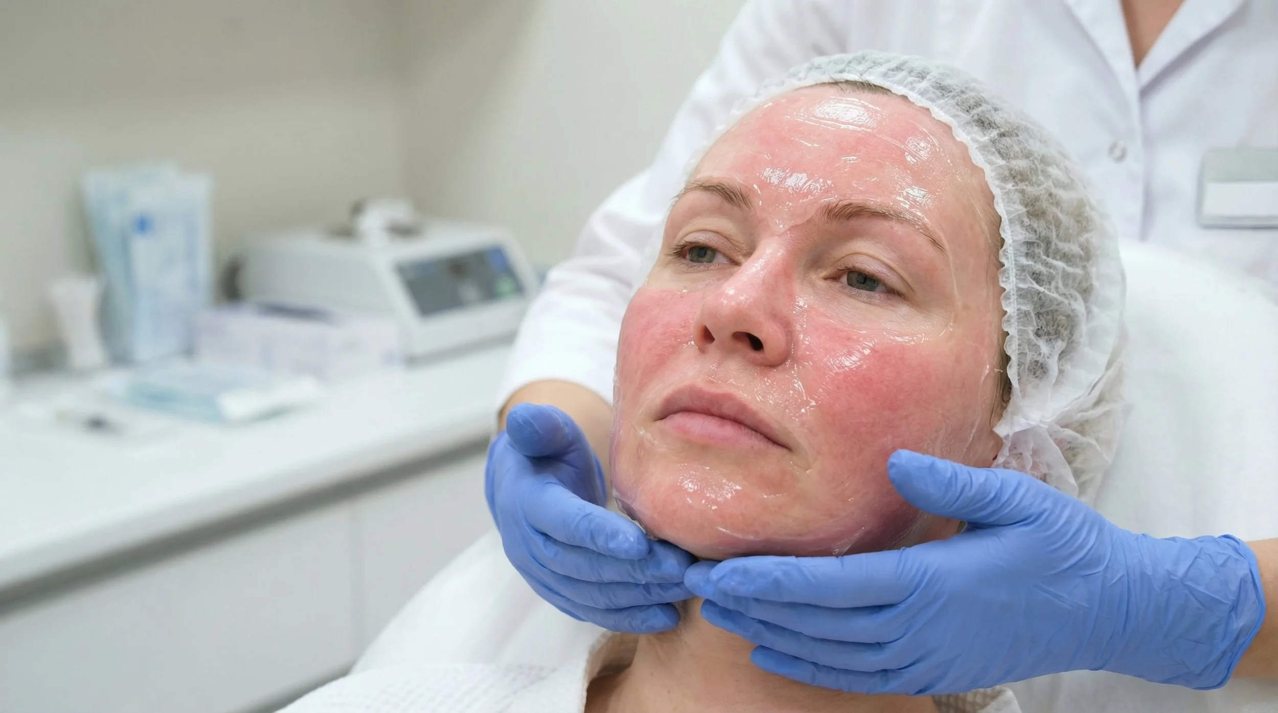 Une femme reçoit un soin du visage dans un cabinet médical, un professionnel en blanc applique un traitement sur son visage.