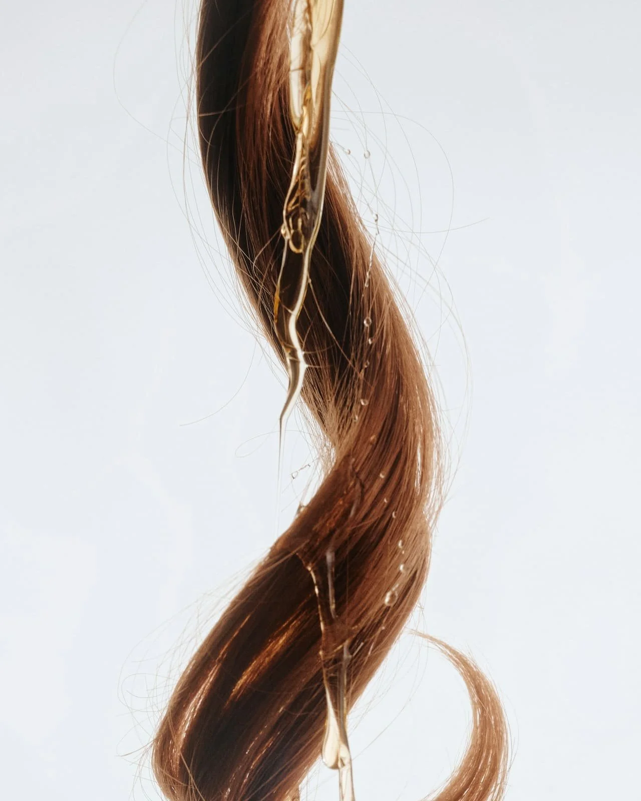 Cheveux bruns mouillés avec des gouttelettes d'eau suspendues, vue en gros plan contre un fond blanc.