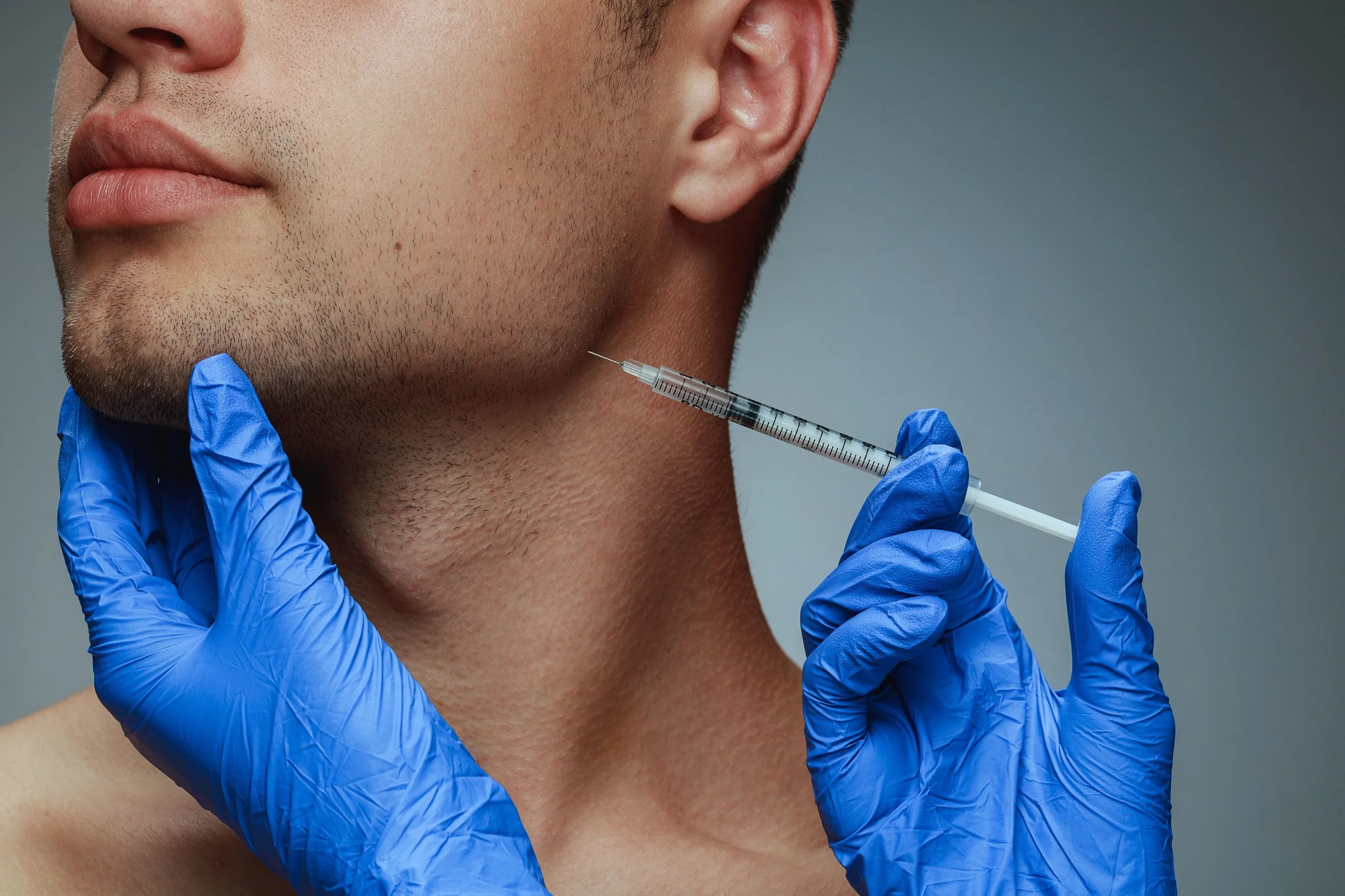 Un professionnel portant des gants bleus injecte un produit dans le visage d’un homme dans un cadre médical.