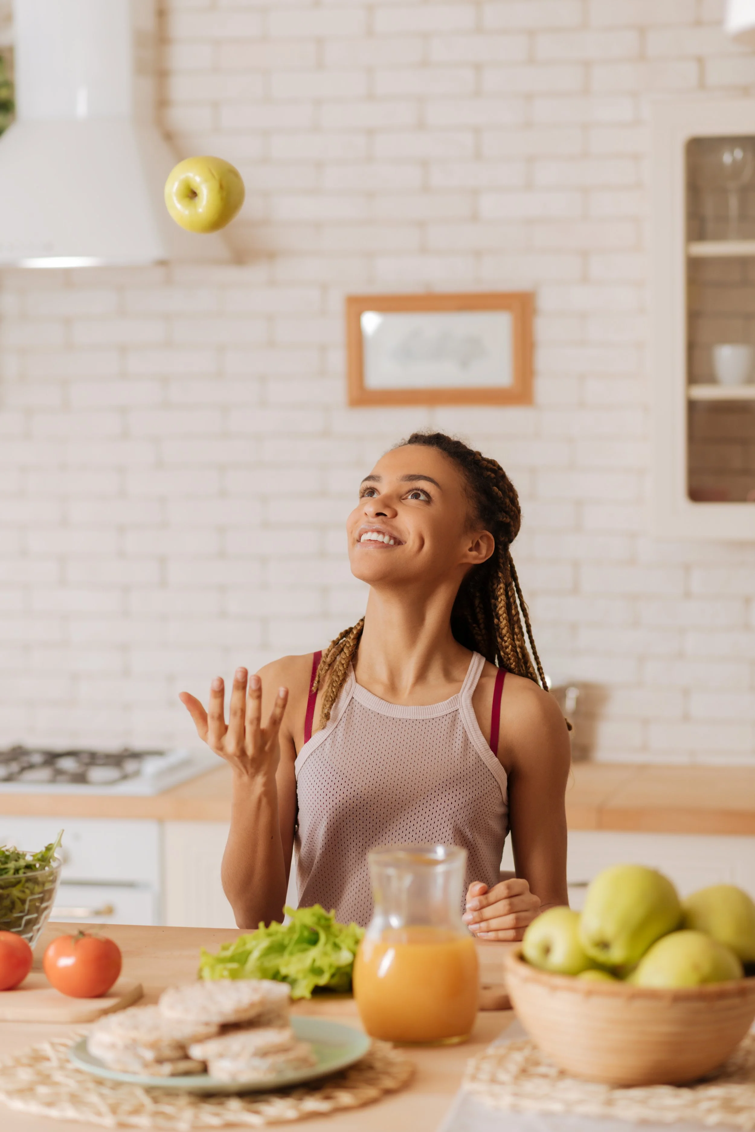 Une jeune femme souriante dans une cuisine moderne, entourée de fruits et légumes frais sur la table.