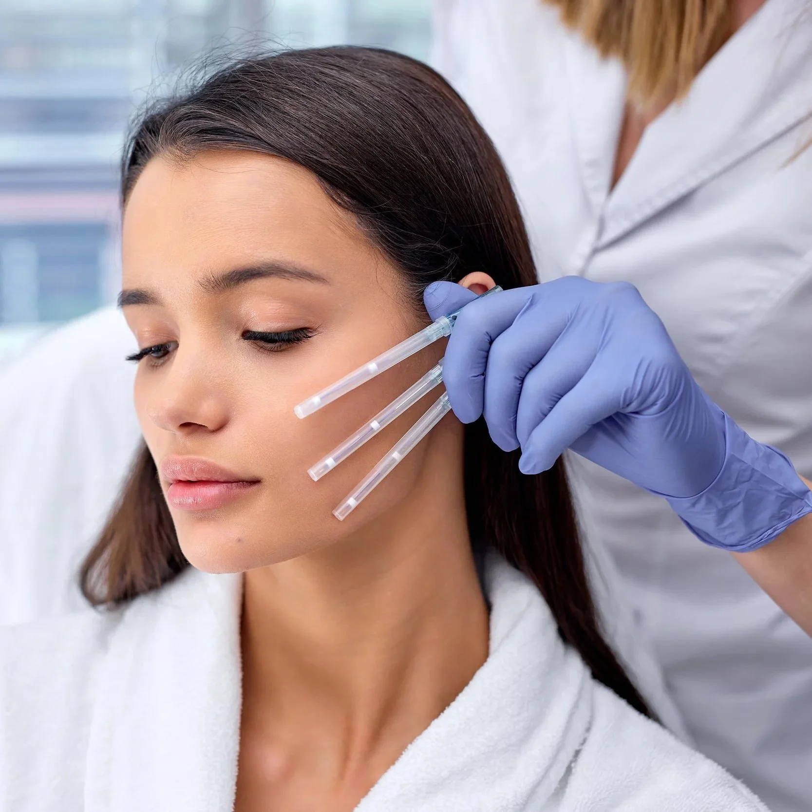 Une femme reçoit une injection sous-cutanée dans la face, administrée par une infirmière portant des gants bleus, dans un environnement médical.