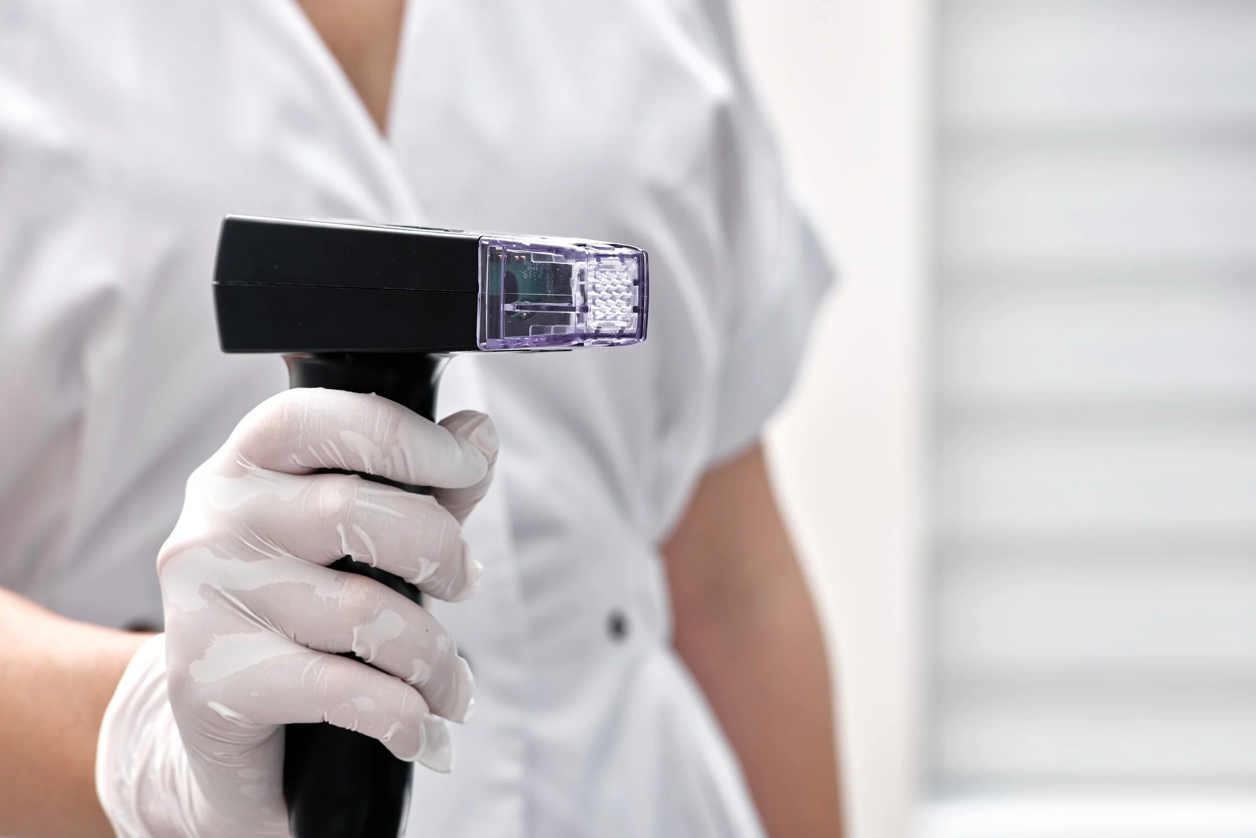 Une personne en blouse blanche et gant blanc tient un appareil de diagnostic médical dans un environnement clinique.