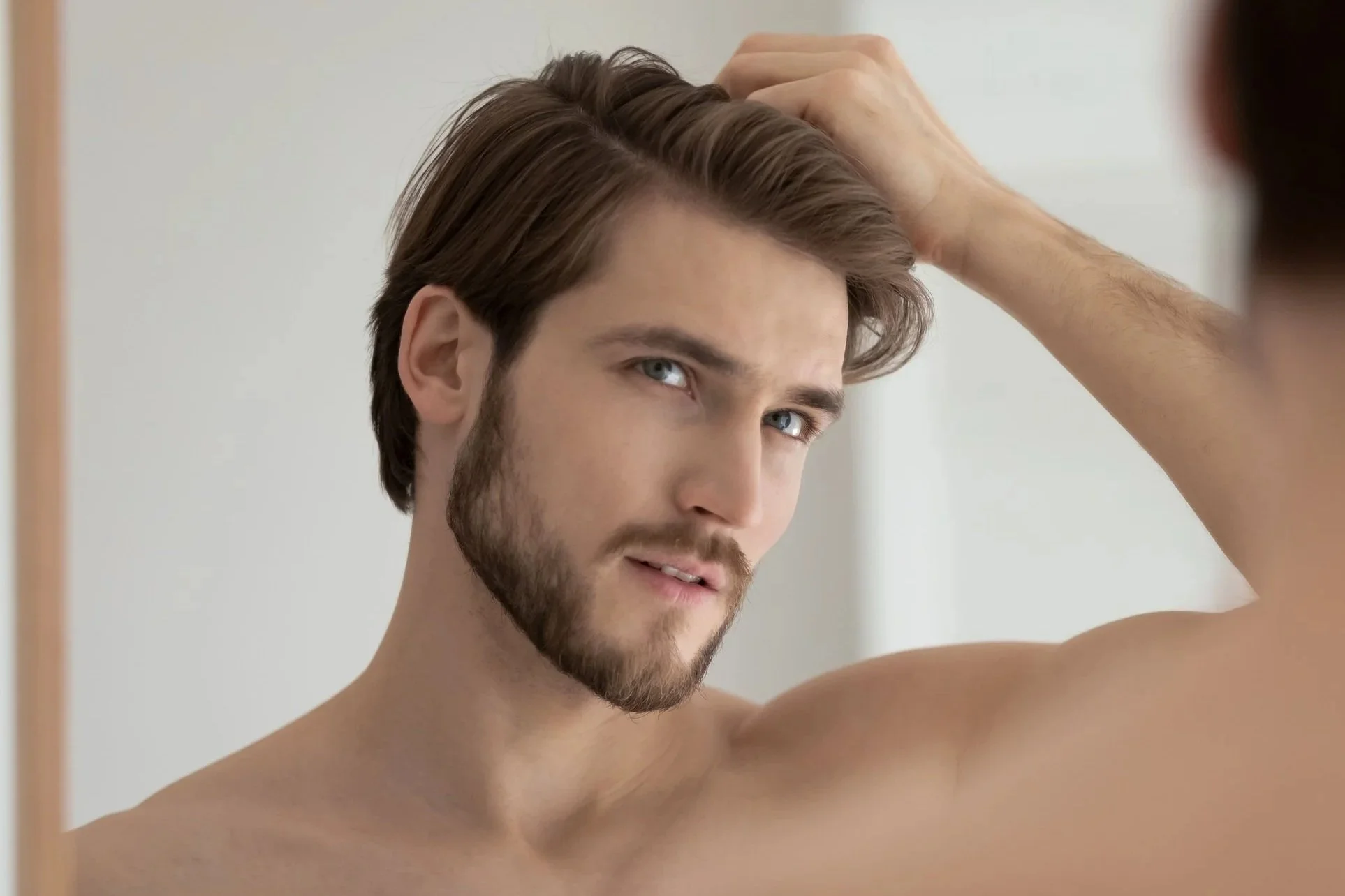 Jeune homme avec barbe et cheveux marron, se regardant dans un miroir.