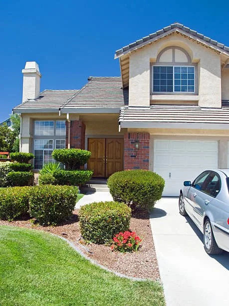 Front view of a two-story suburban house with a manicured lawn, shrubs, and a parked car