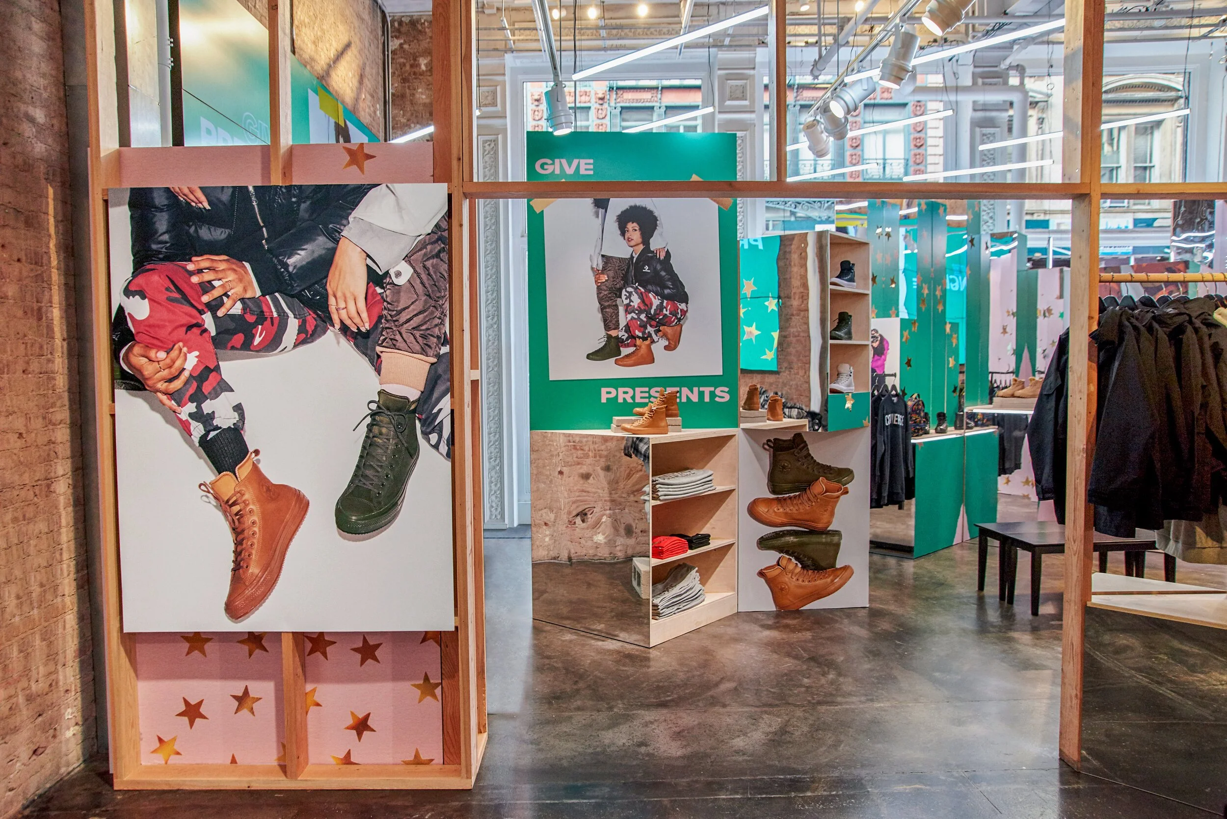 Inside a retail store, display shelves showcase various styles of boots. Large promotional posters featuring models wearing boots are visible, with one poster showing a close-up of the shoes and a model squatting. Bright lighting and turquoise and pink decorative panels add to the store's lively atmosphere.