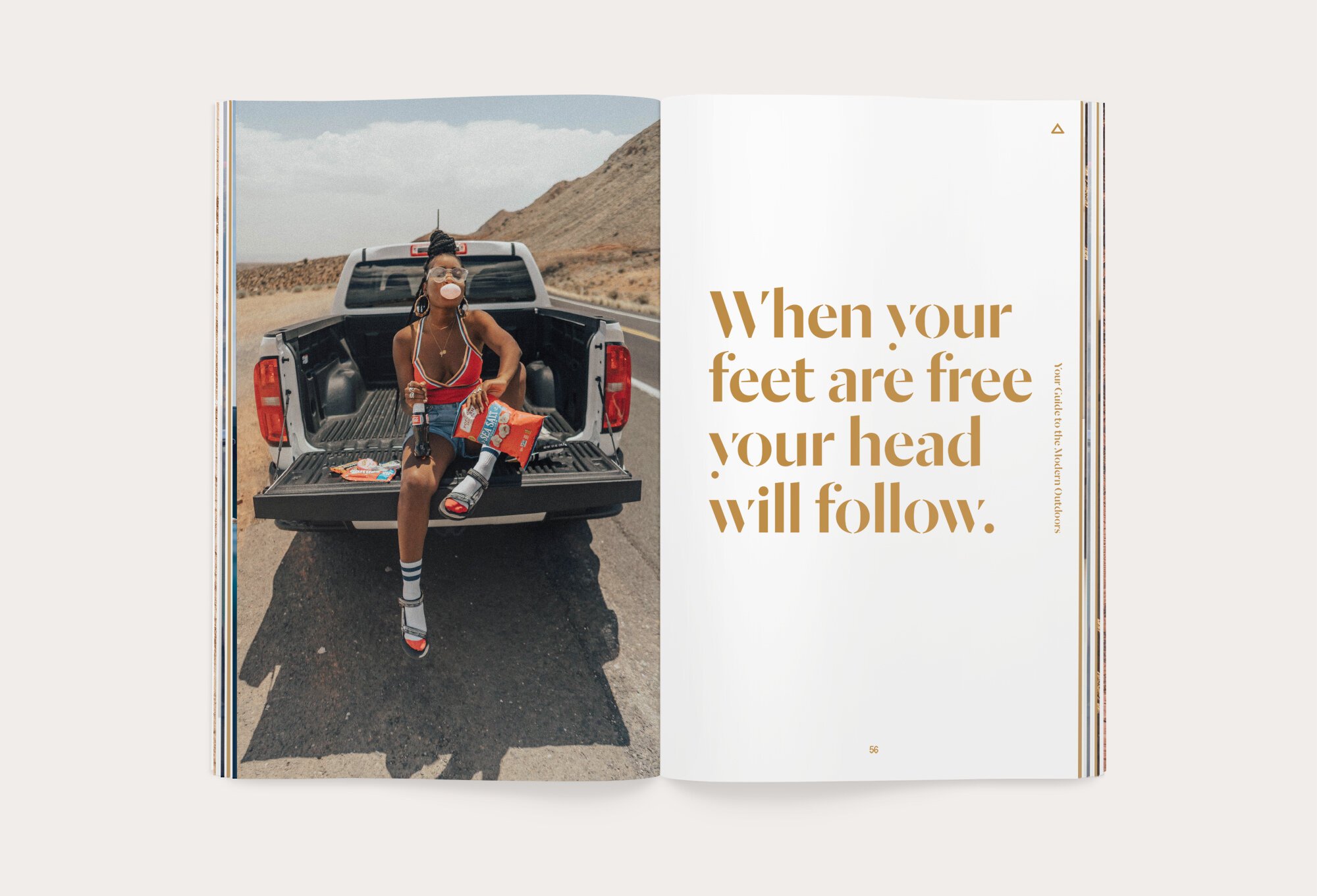 A woman sitting on the tailgate of a pickup truck on a remote road in a desert landscape, wearing a red tank top, shorts, and sneakers, blowing bubble gum, surrounded by snacks.