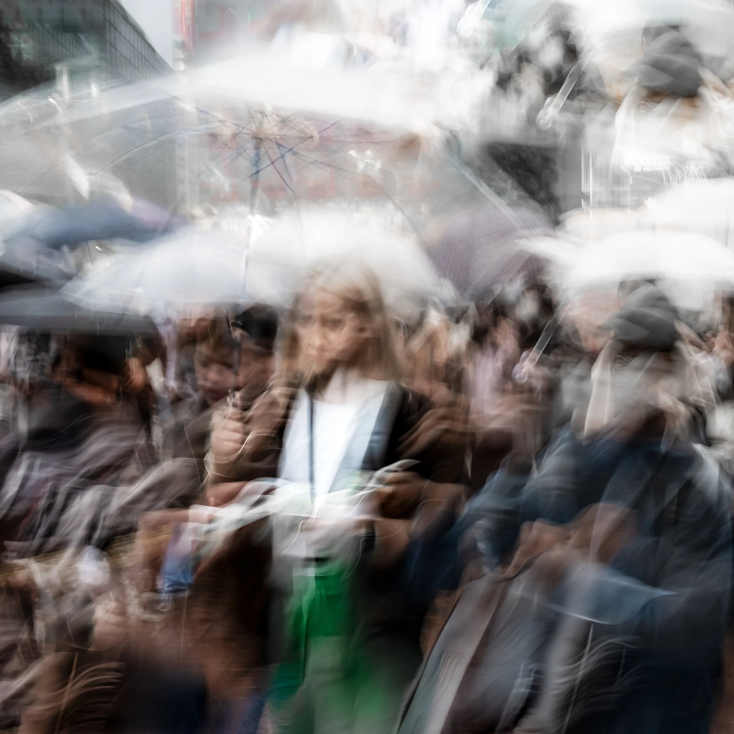 A blurred crowd of people holding umbrellas in the rain.