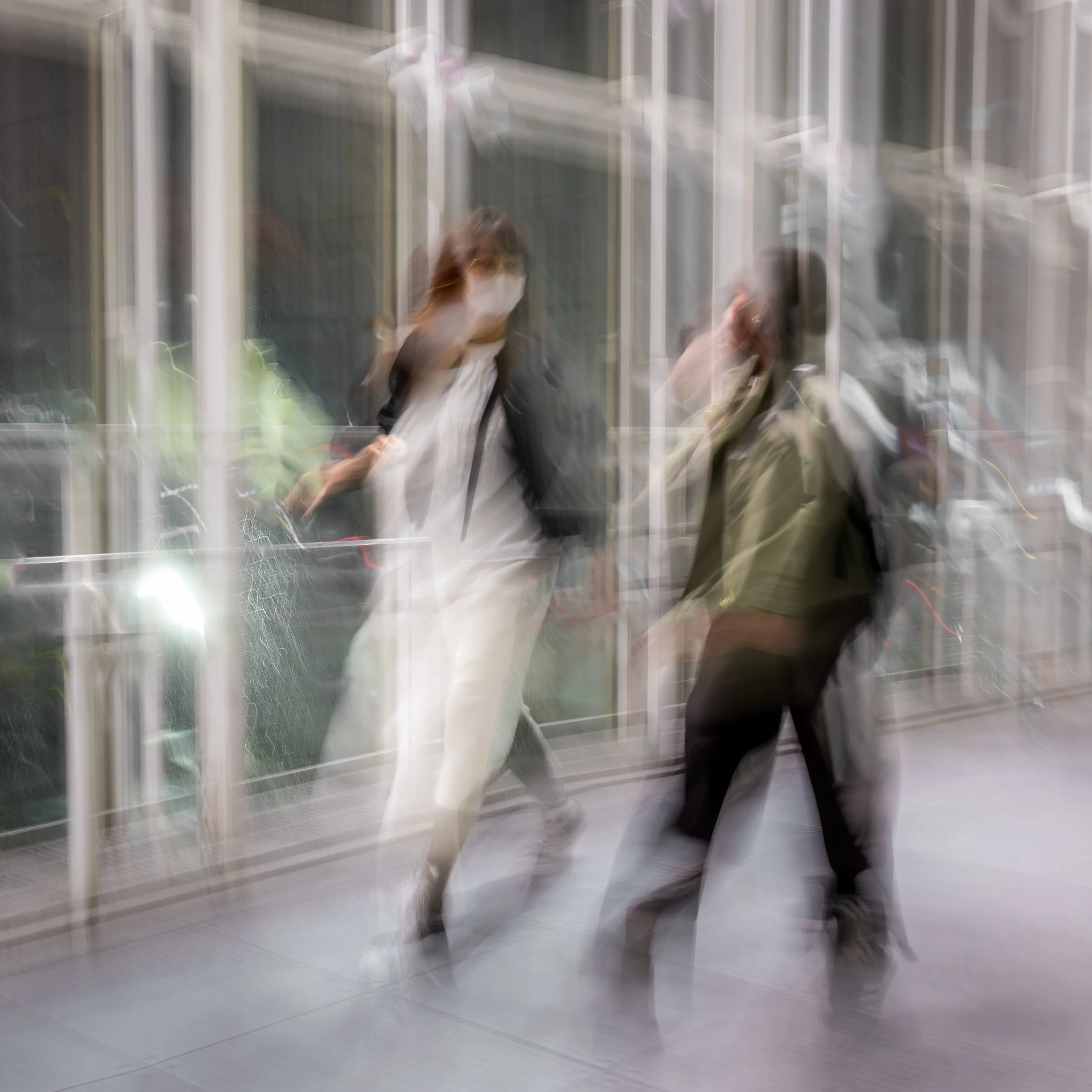 Two people walking indoors, both wearing face masks, with a blurred motion effect.