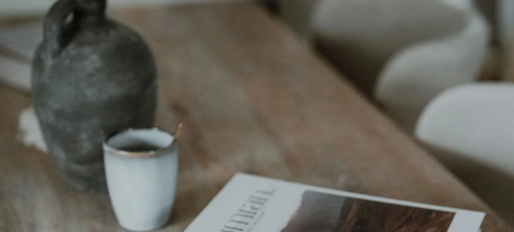 A wooden table with a rustic vase, a cup of coffee with a spoon, and a magazine.
