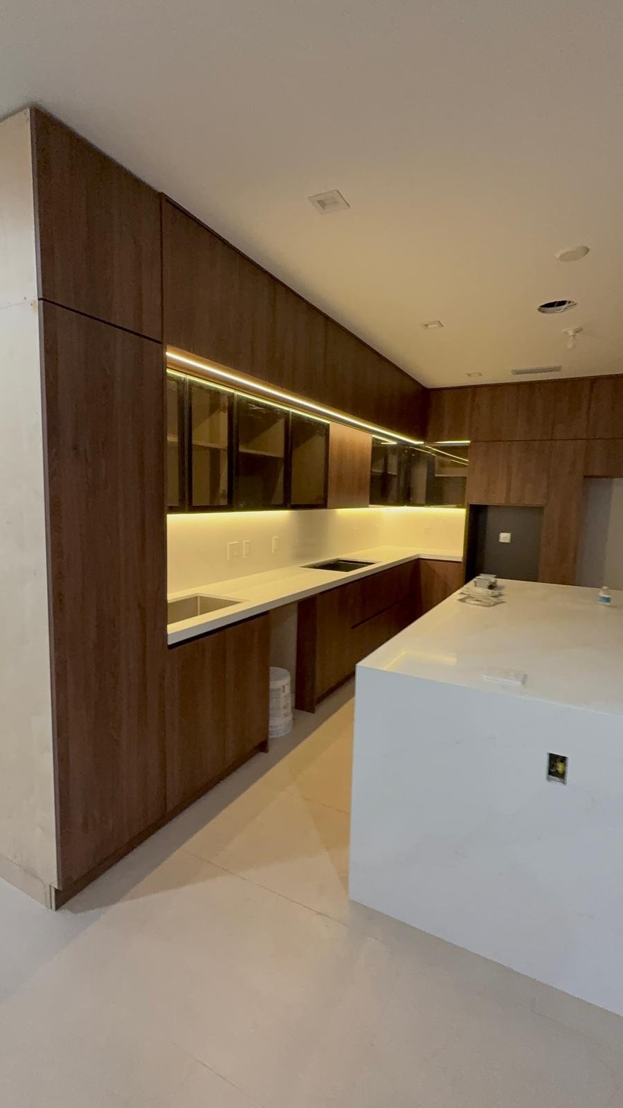 Modern kitchen with dark wooden cabinets, white countertops, and LED lighting.