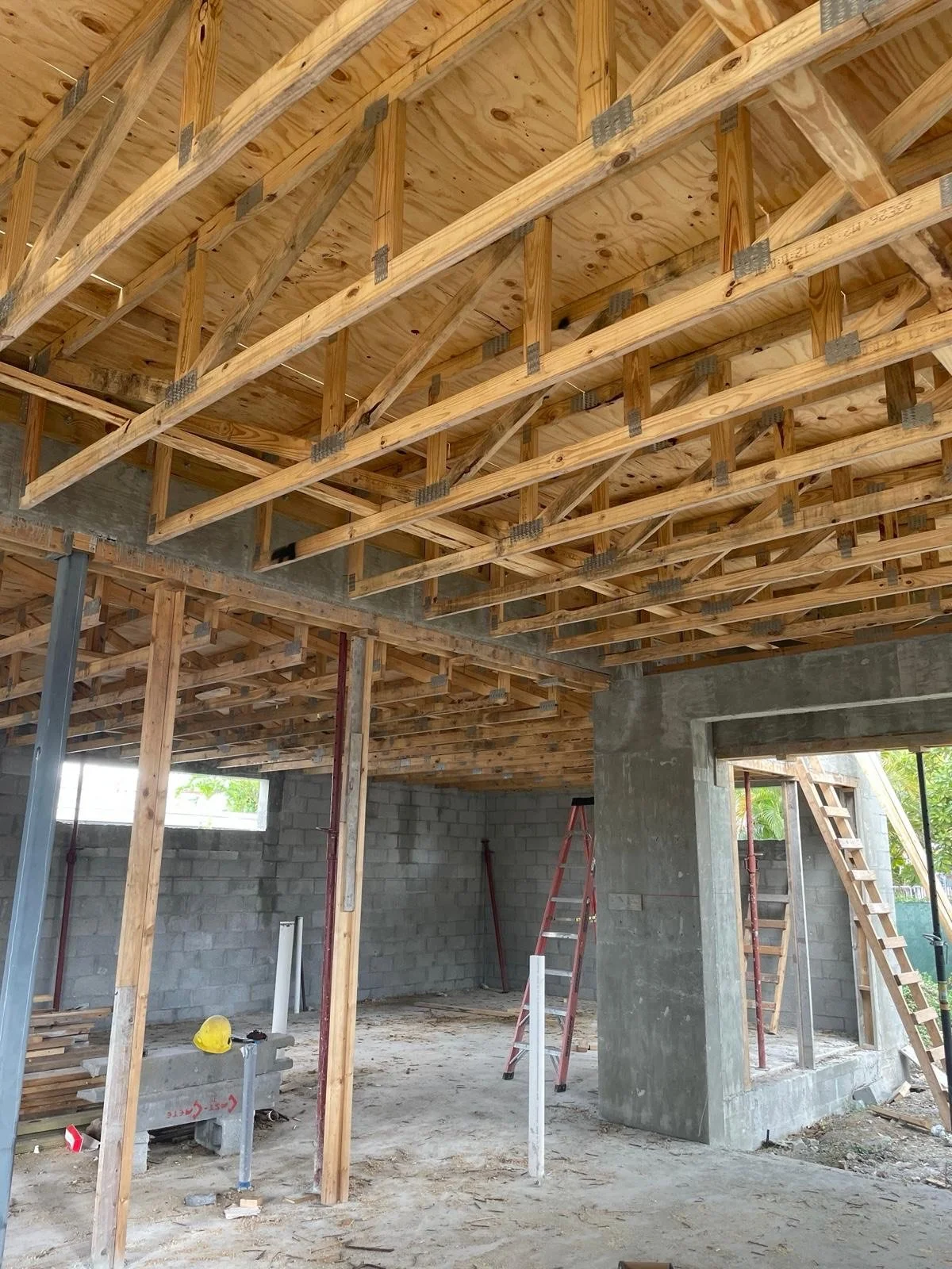 Interior view of a building under construction showing wooden framing, concrete block walls, scaffolding, and a ladder.