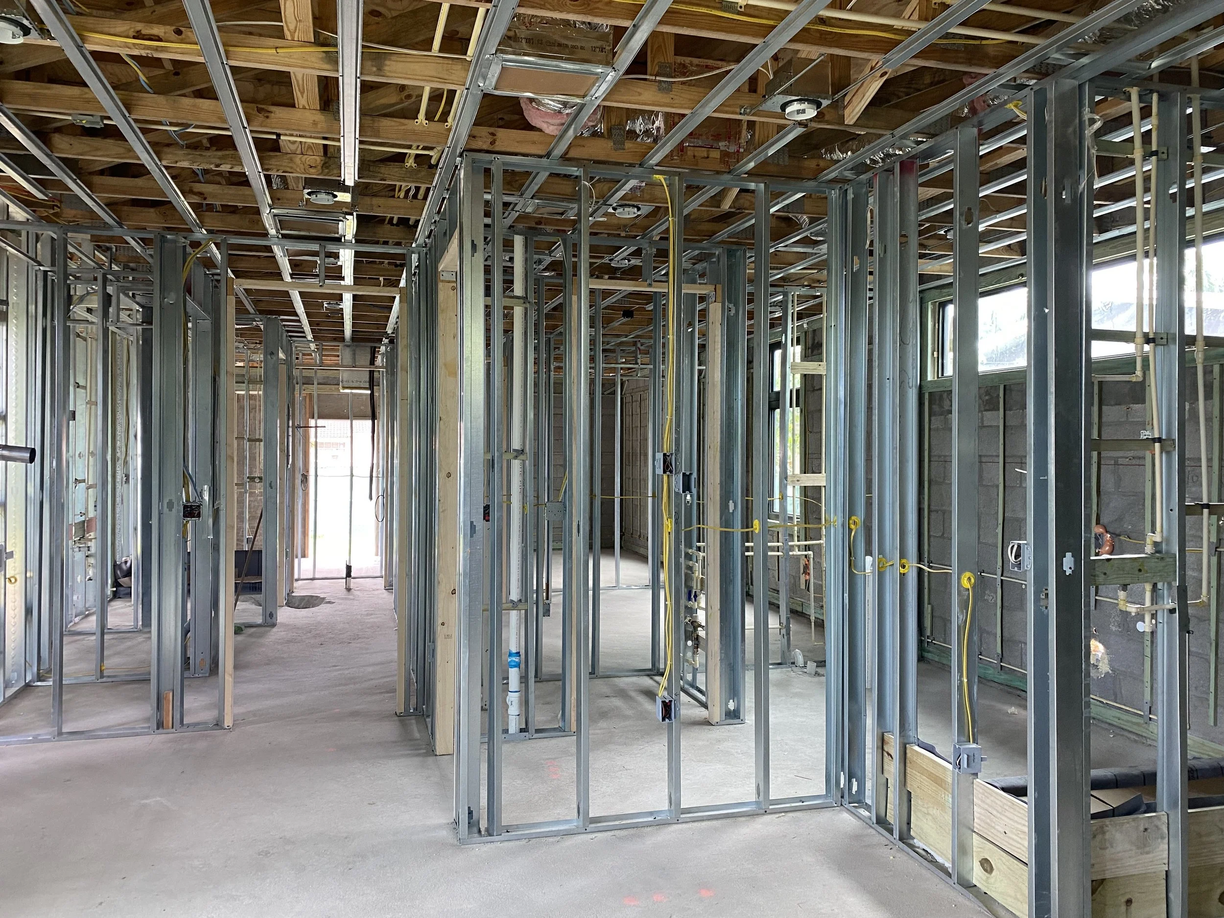 Interior of a house under construction showing metal framing, electrical wiring, and unfinished ceiling with exposed wood and insulation.