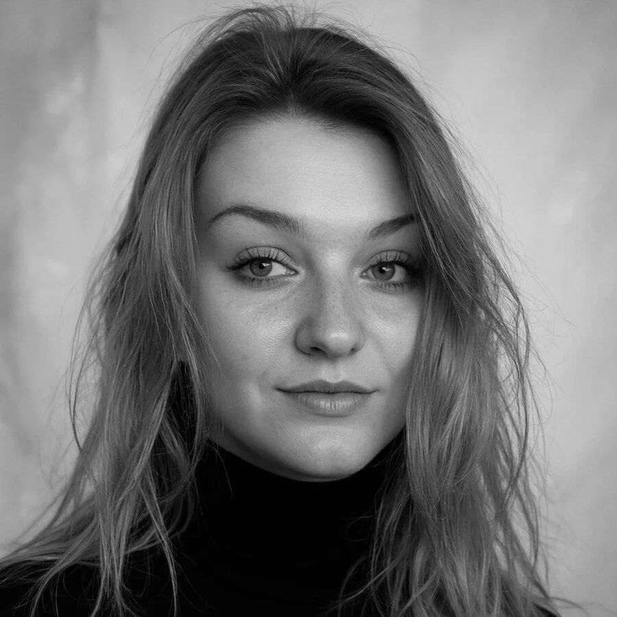Black and white portrait of a young woman with wavy hair, wearing a black turtleneck, looking directly at the camera with a slight smile.