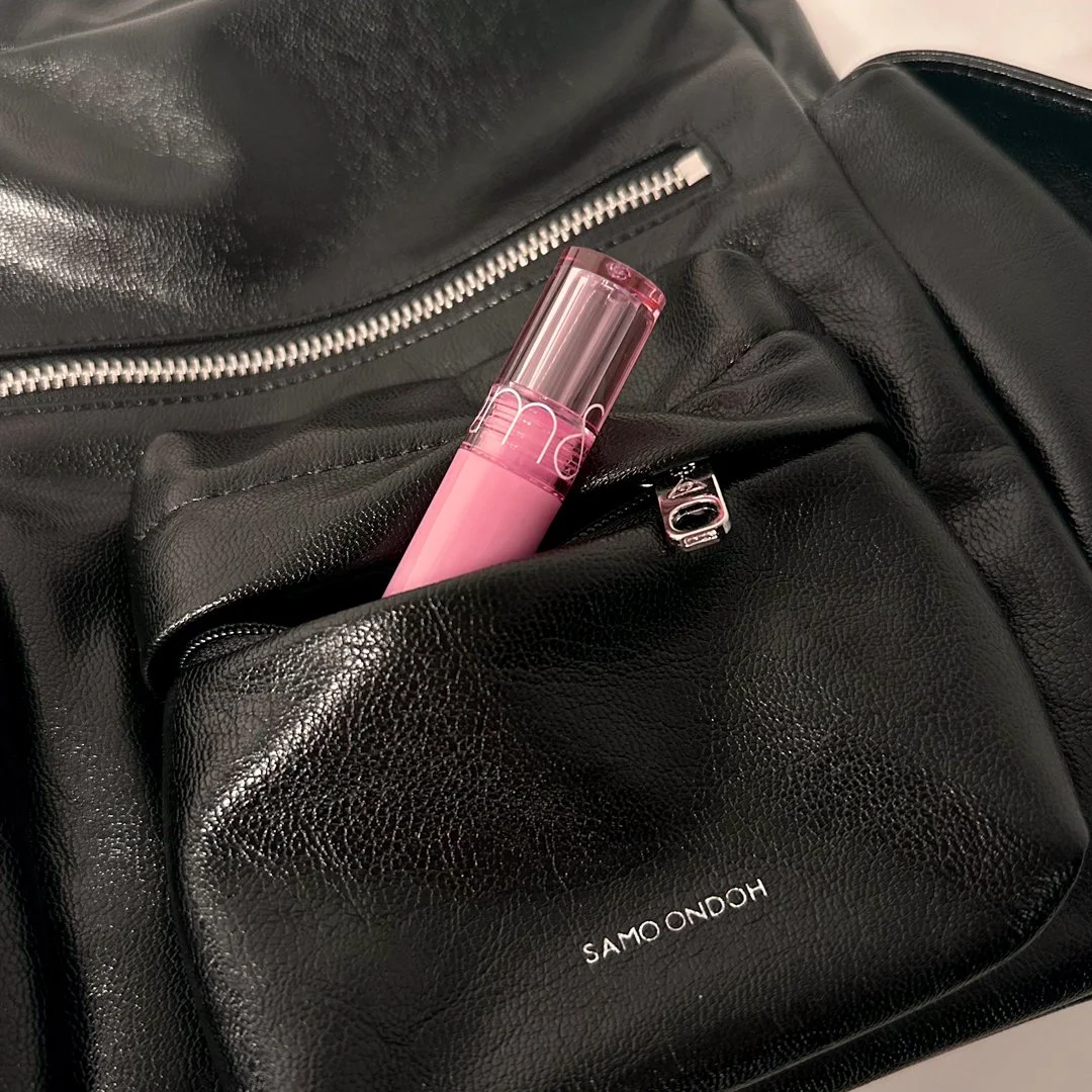 Black leather bag with a pink lip gloss tube inside a front pocket.