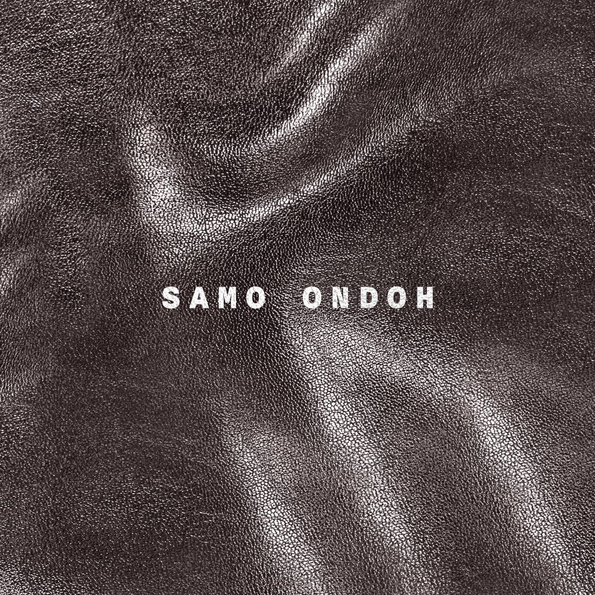 Close-up of dark brown textured leather surface with white text 'SAMO ONDOH' in the center.