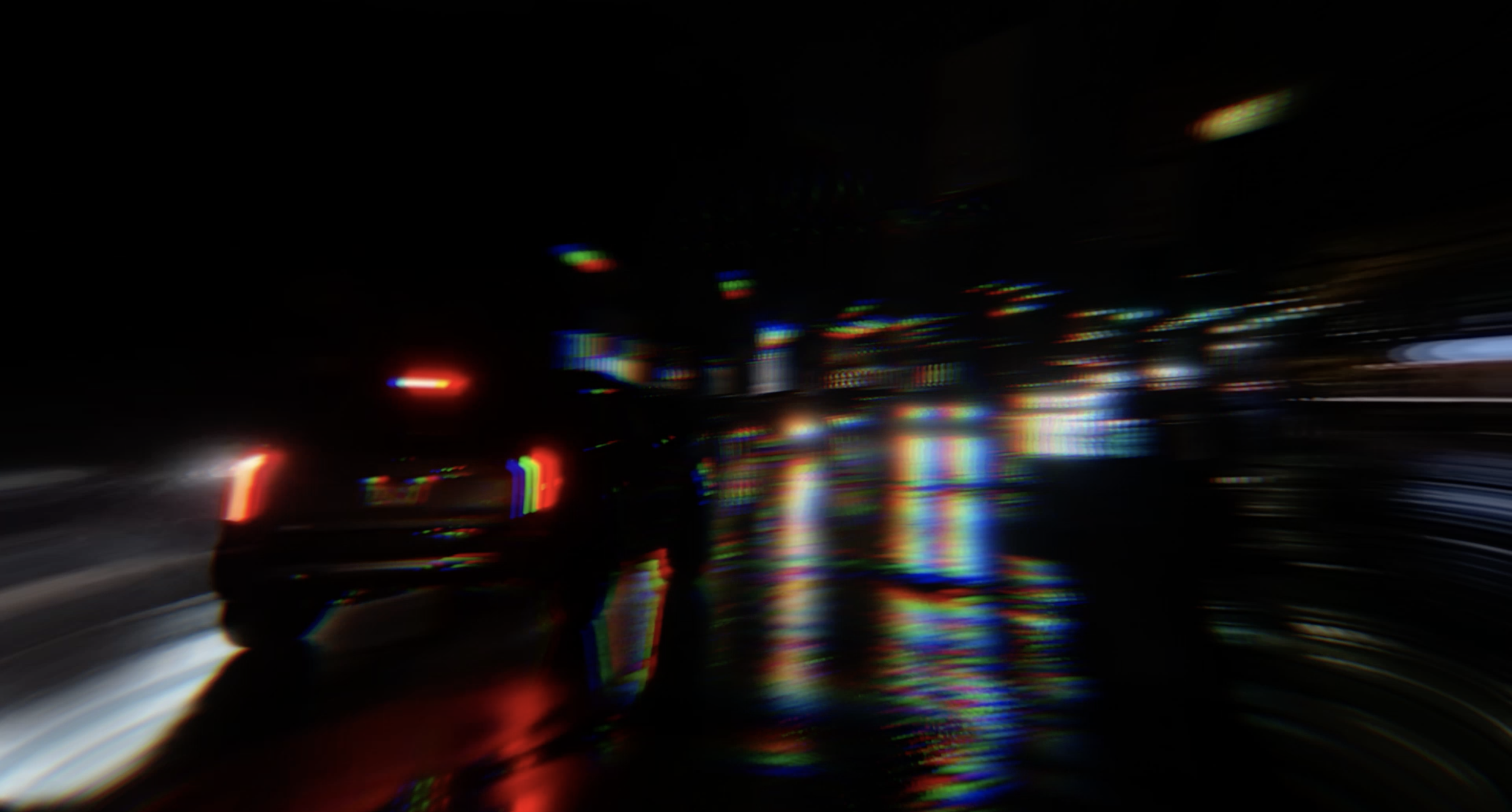 Blurred nighttime city street scene with light reflections and a silhouette of a person walking.
