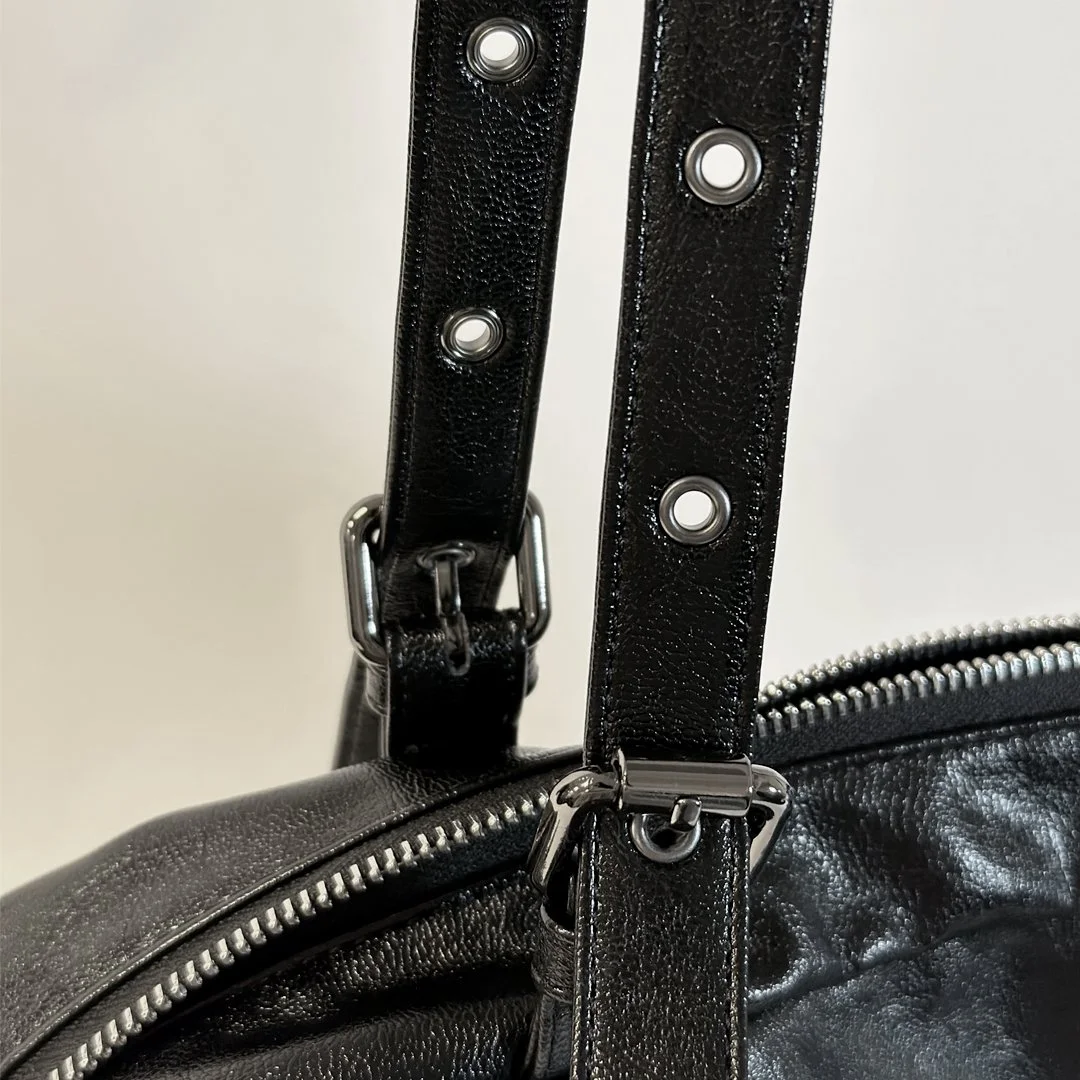 Close-up of a black leather handbag with metallic hardware and adjustable straps.