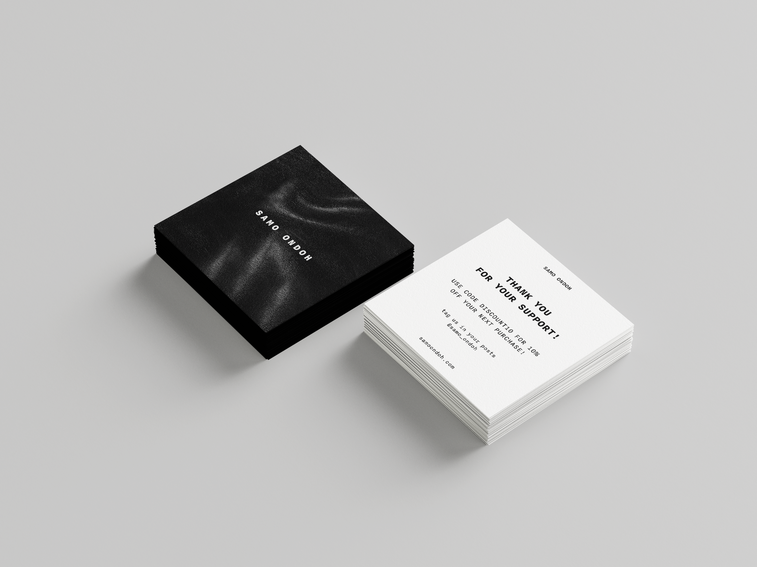 Stack of black business cards and a stack of white thank you cards on a light gray surface. The black cards have white text, and the white cards have black text.
