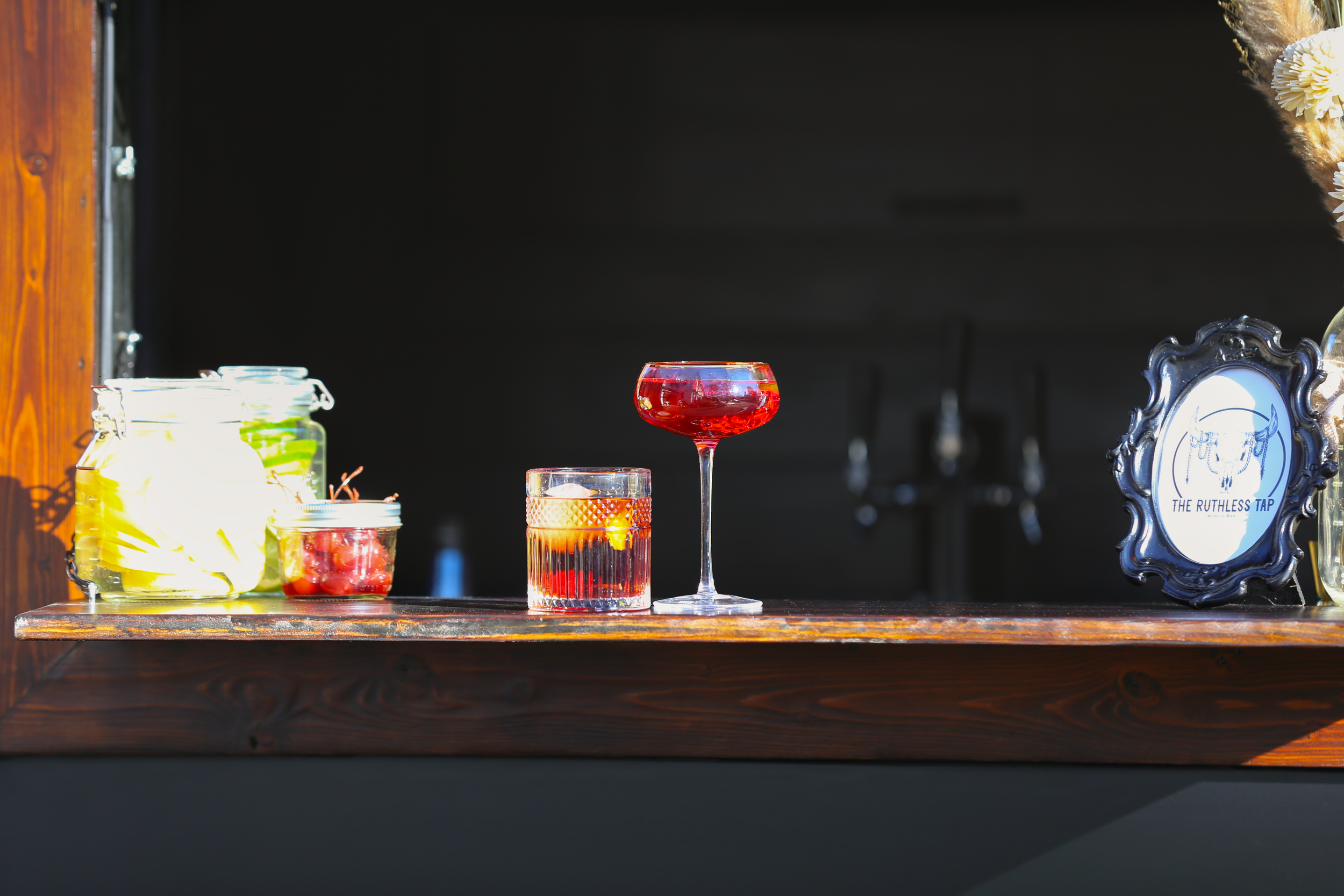 Table with jars of fruit, two cocktails, and a framed sign that reads 'The Ruthless Tap'