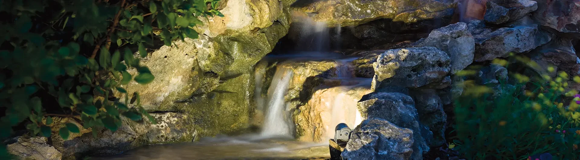 Small waterfall flowing over rocks surrounded by greenery in a natural setting.